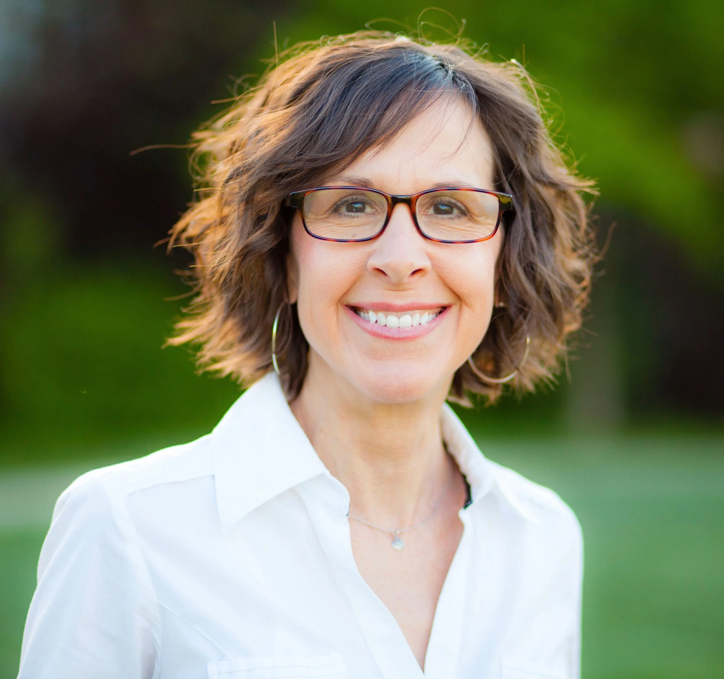 Person with brown hair and glasses smiling with a white shirt in front of a green background