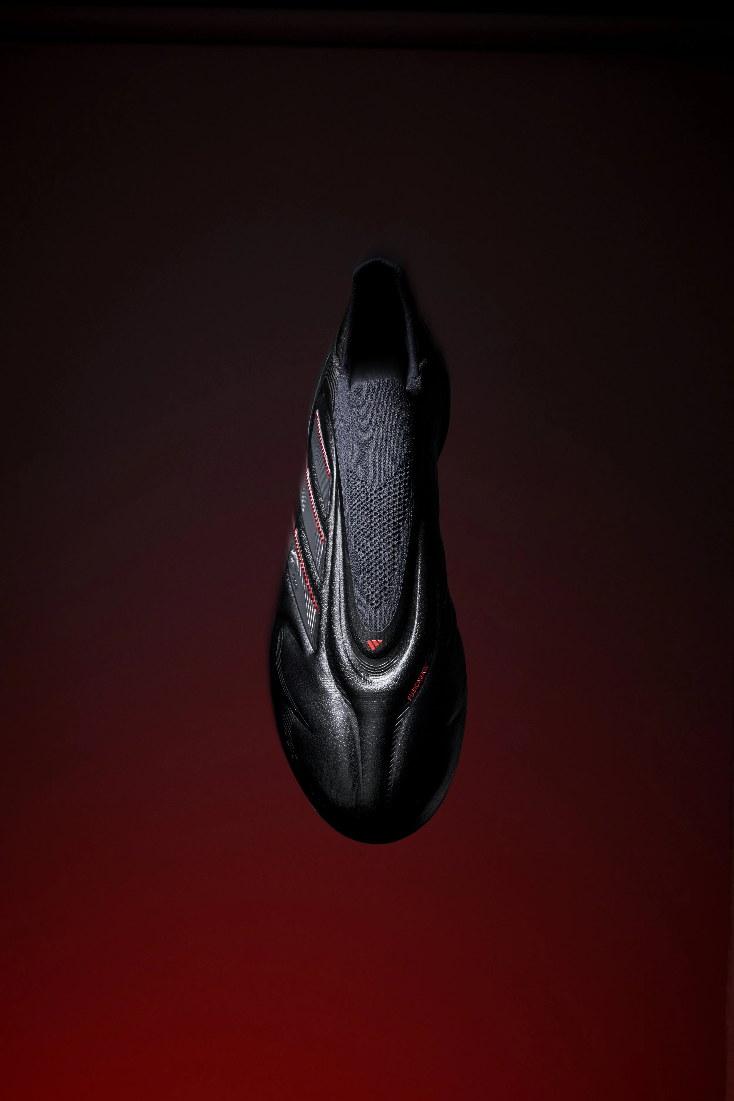 A black cycling shoe with red accents, displayed against a dark red background with a gradient effect.