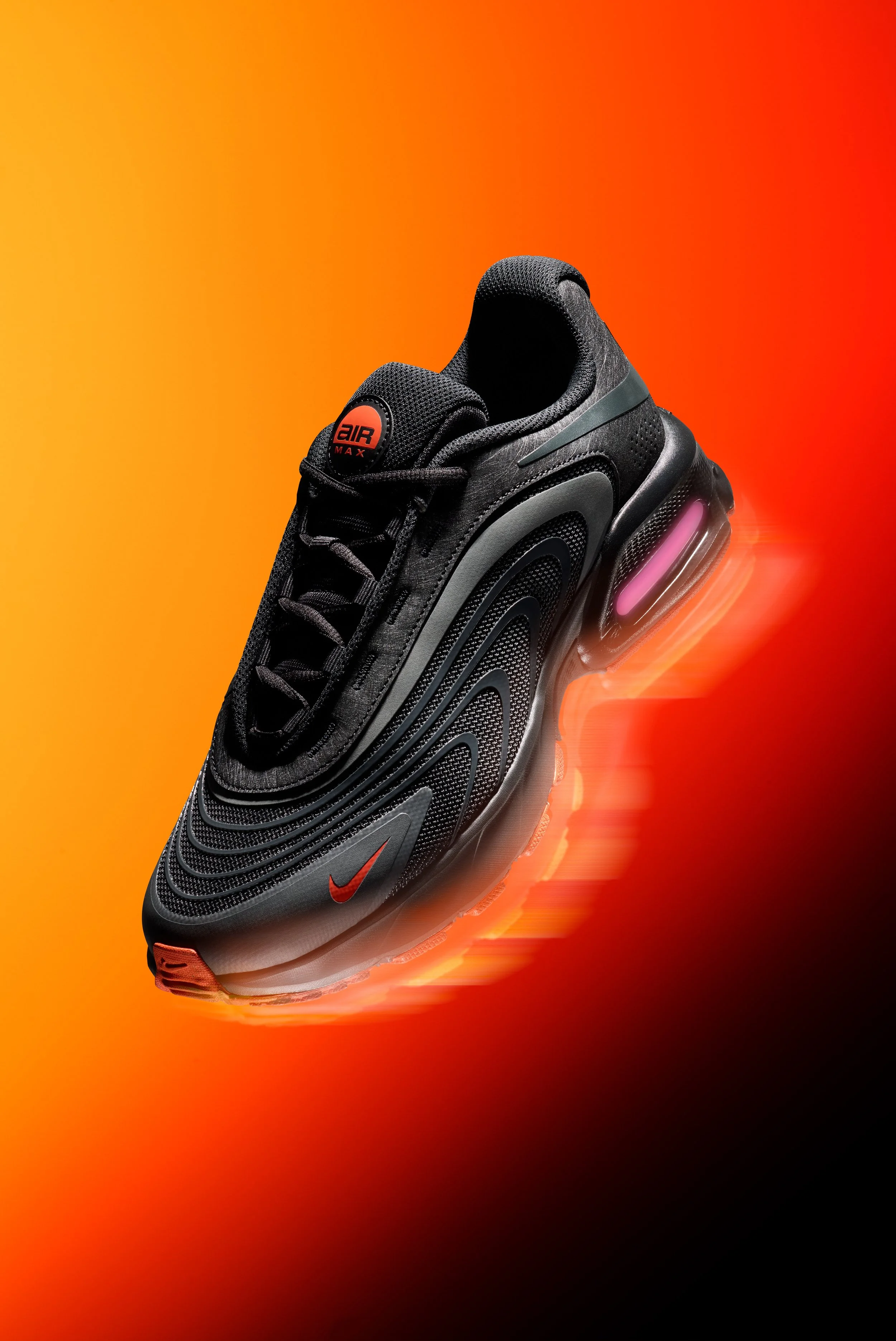 A black Nike Air Max sneaker with a glowing pink air cushion, set against a vibrant orange and red background.