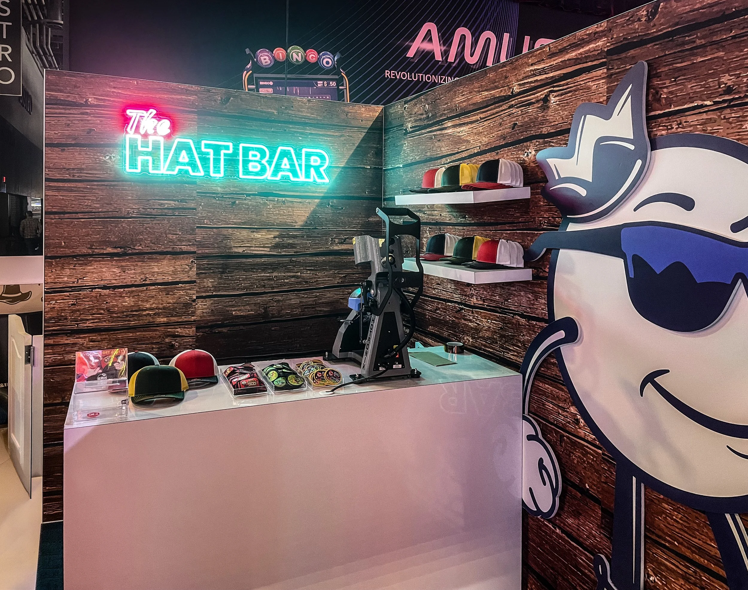 A retail display with a neon sign reading 'The Hat Bar,' hats on shelves, and a large cartoon mascot wearing sunglasses giving a thumbs-up.