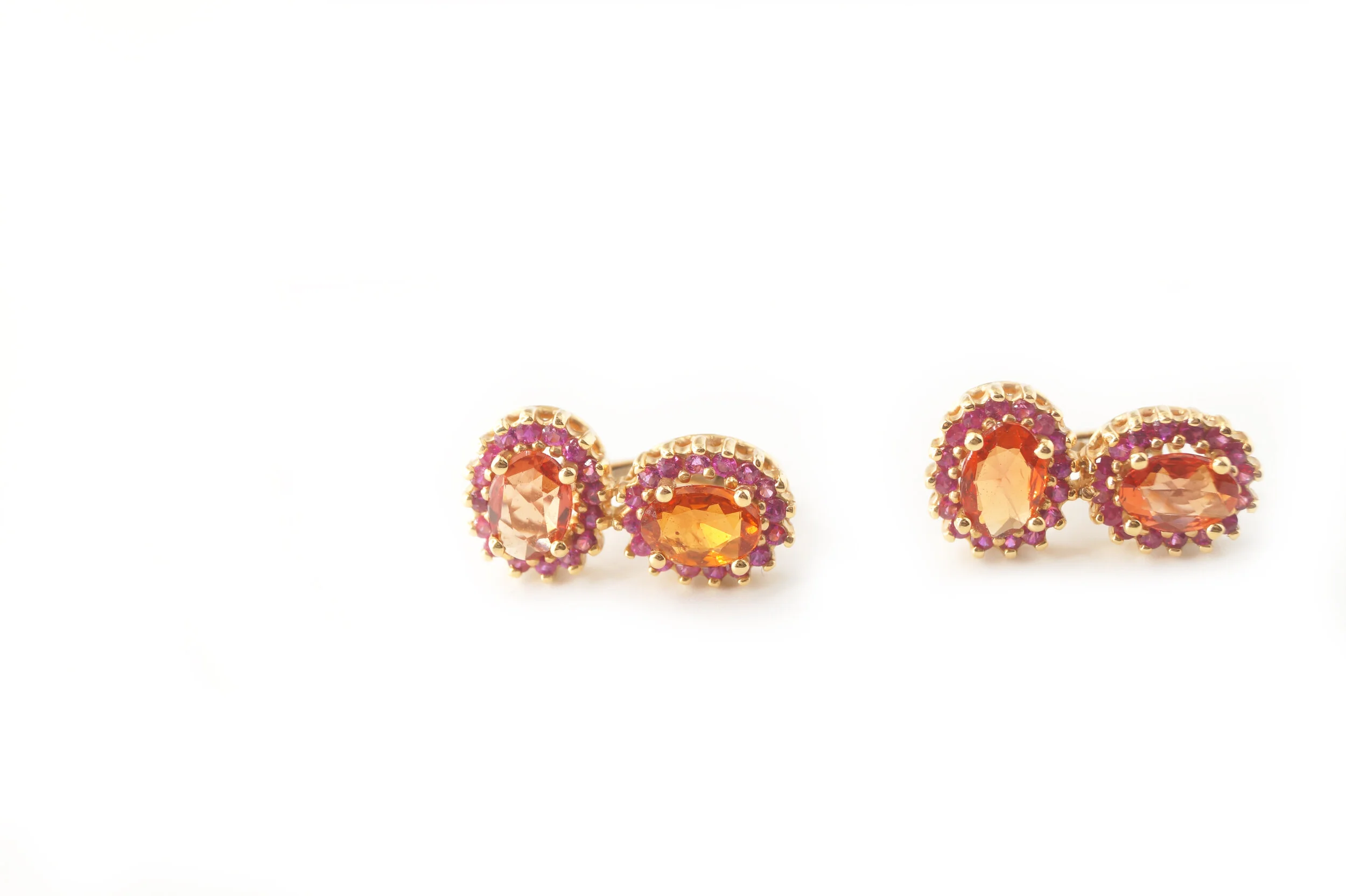  Larra Tops   $9,200.00      A pair of eighteen-karat yellow gold convertible earrings, each set with two orange sapphire ovals – the top set vertically and the bottom set horizontally.  These two gems have been surrounded with an entourage of pink d