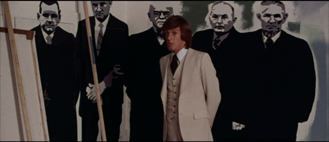 Thom (Michael Greer) stands before one of Arletty’s father’s paintings — suit-clad men who eerily resemble the film’s flesh-eating ghouls.