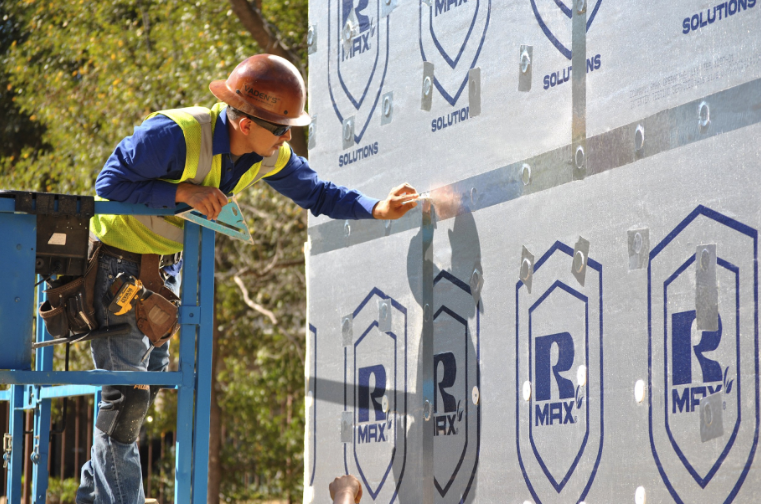 Worker installing exterior fireproof insulation panels on a commercial building wall.