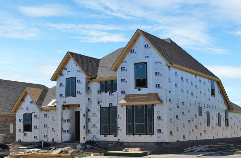 House under construction wrapped in insulation sheathing with a steep shingle roof.