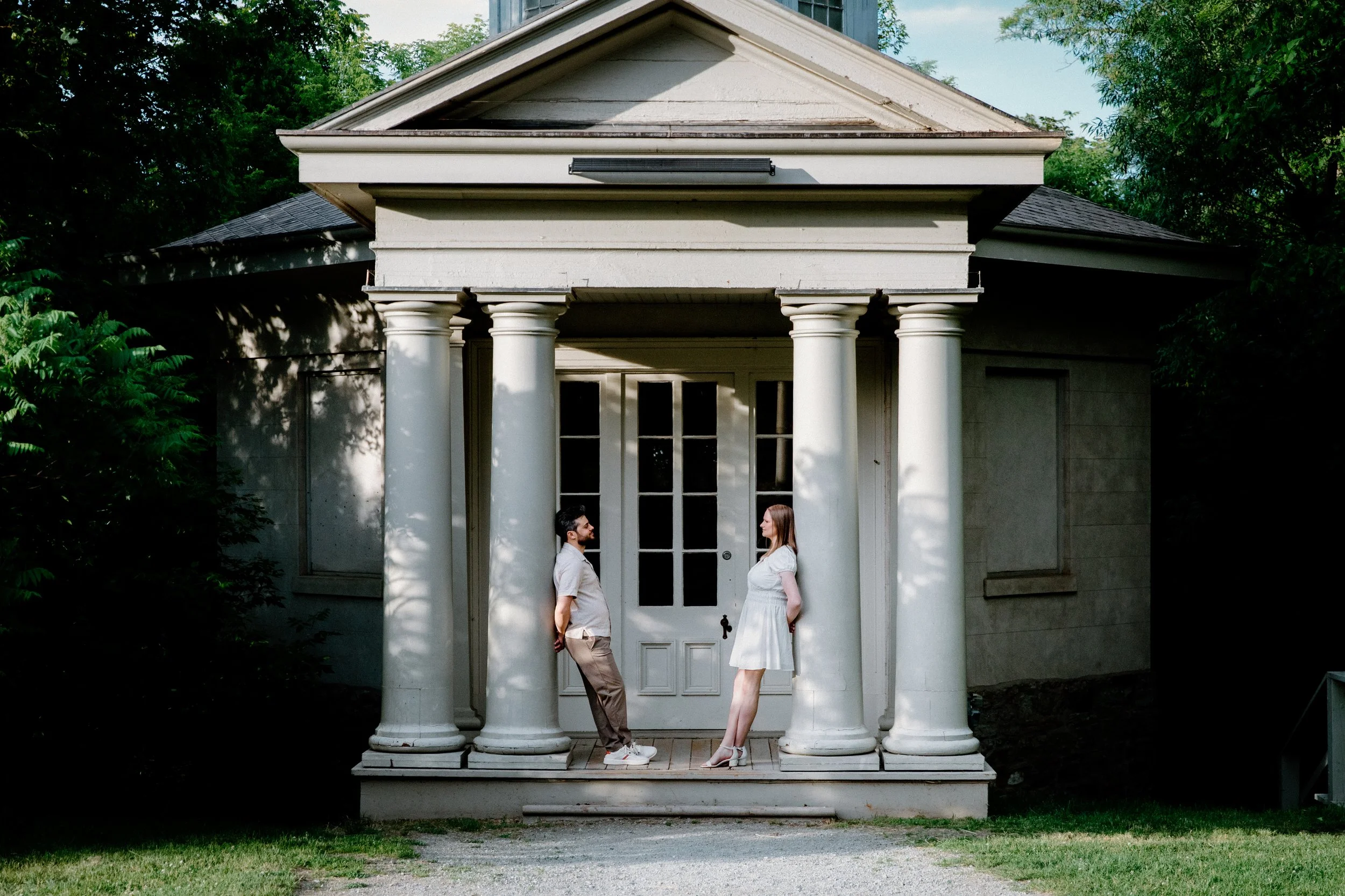 Editorial inspired engagement portrait of a couple standing at opposite pillars of Dundurn Castle looking at each other