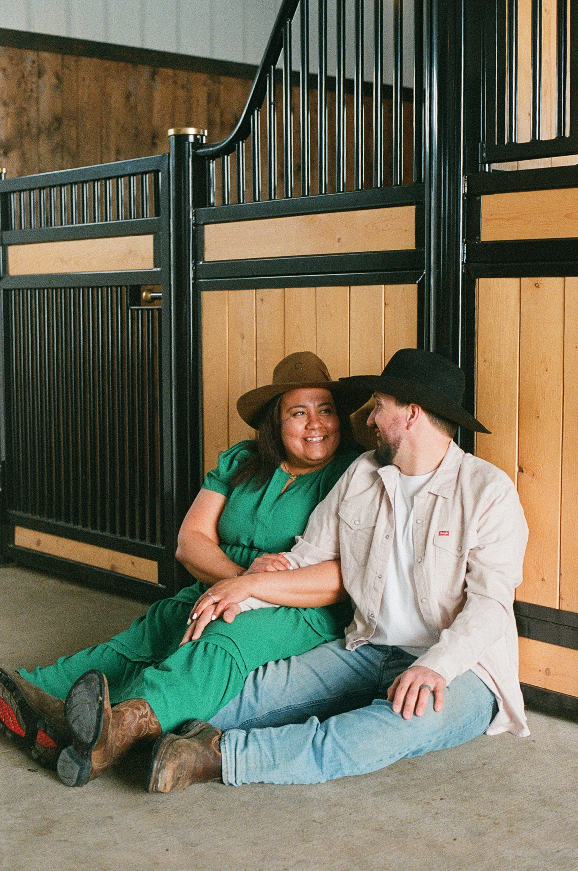 Film photo of a couple sitting together against horse stables at a ranch in Edmonton during their engagement session