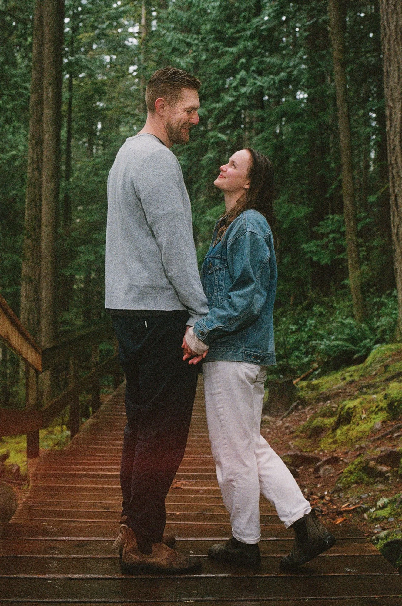 Warm film photograph of a couple looking at each other and smiling during their engagement session in Lynn Valley, Vancouver