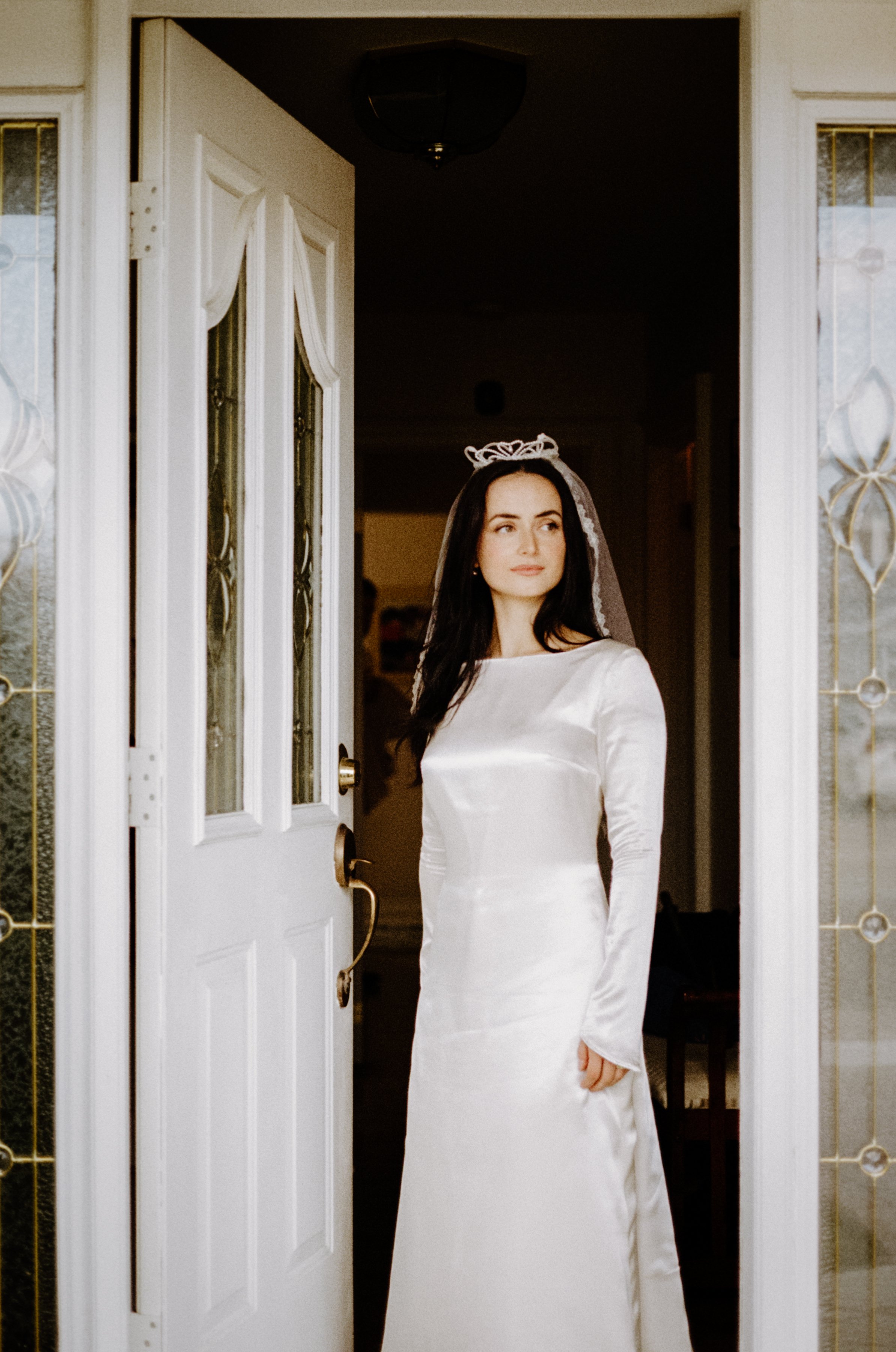 Classic editorial inspired film portrait of a bride standing at the front door of her home on her wedding day in Vancouver