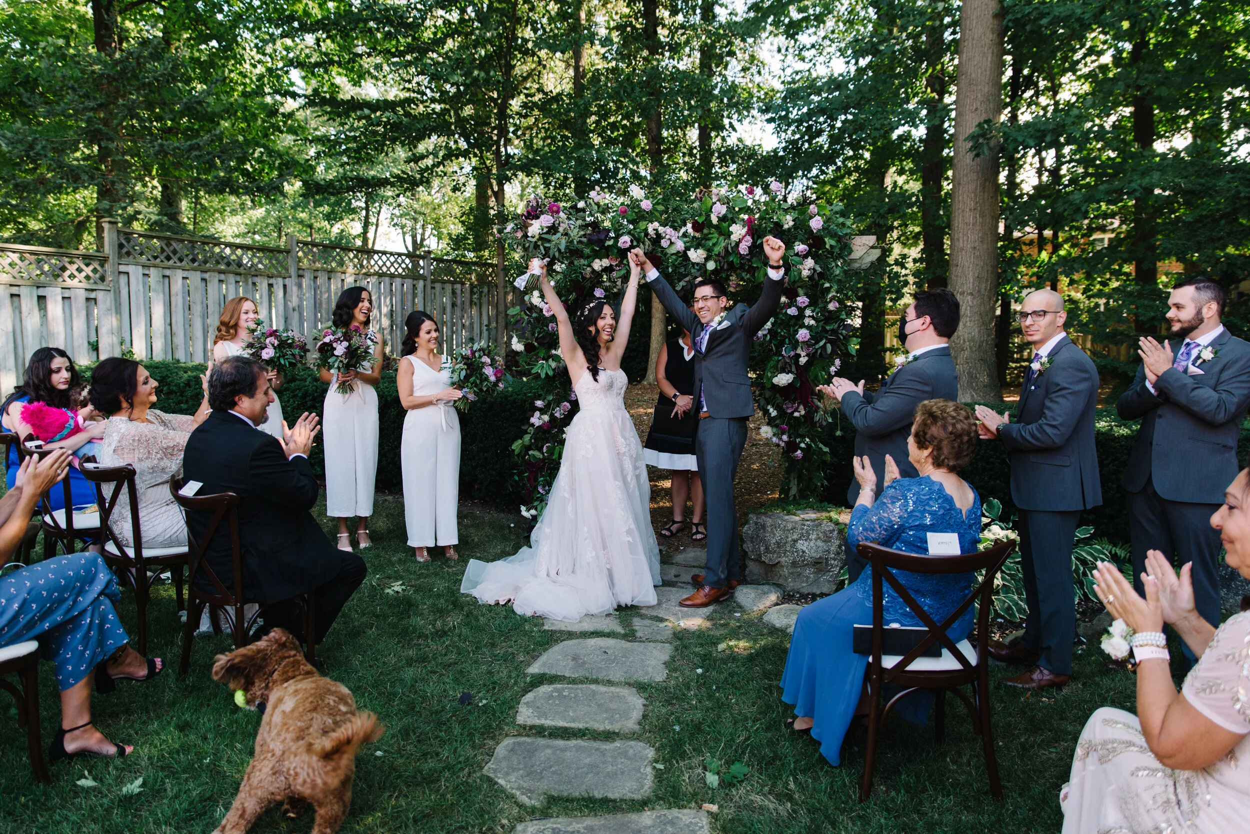 Candid photo of a couple joyfully saying I do during their intimate backyard wedding in Mississauga, with their dog running through the frame and guests cheering around them