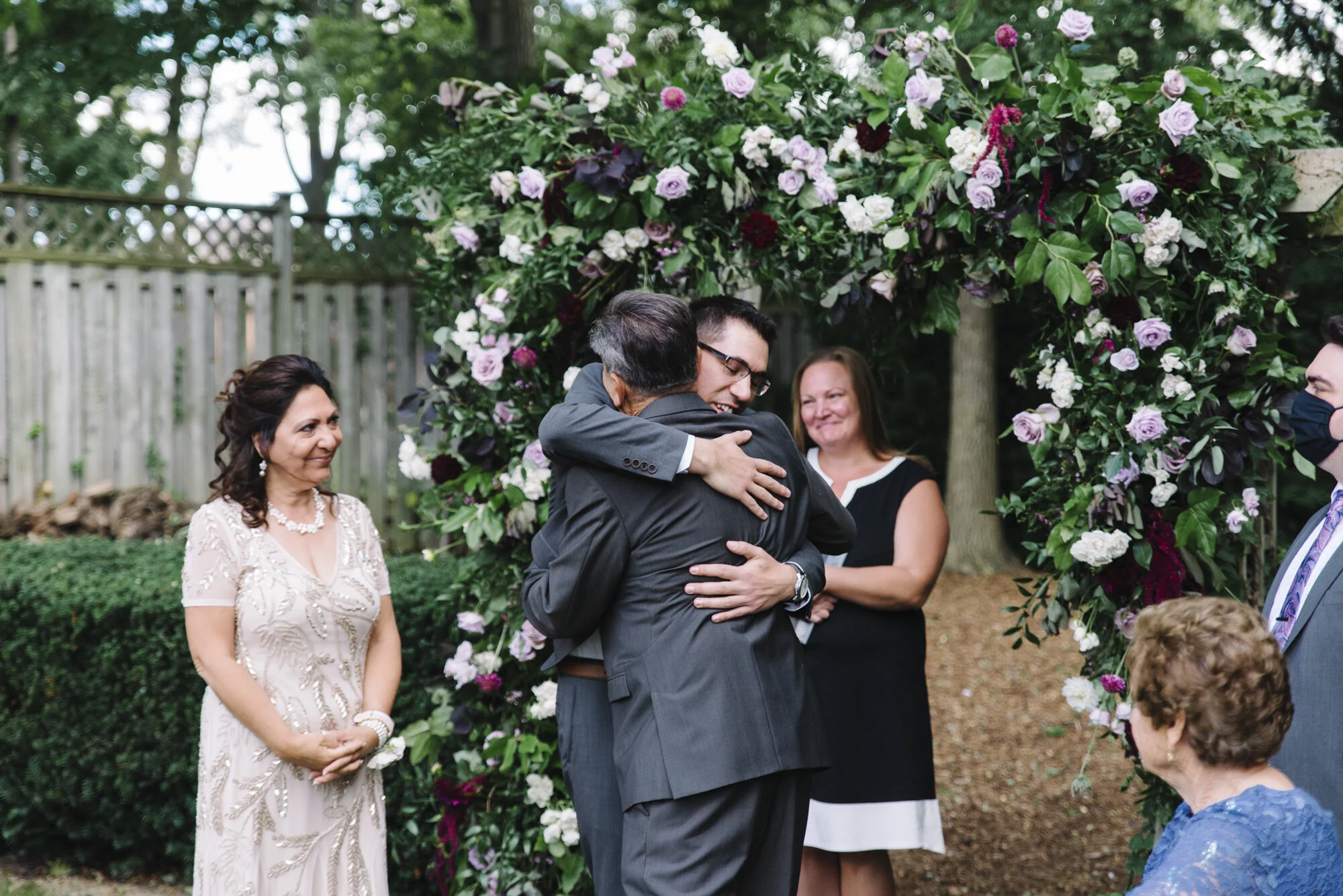 Emotional candid of a groom hugging his bride's parents as they give her away at an intimate backyard wedding