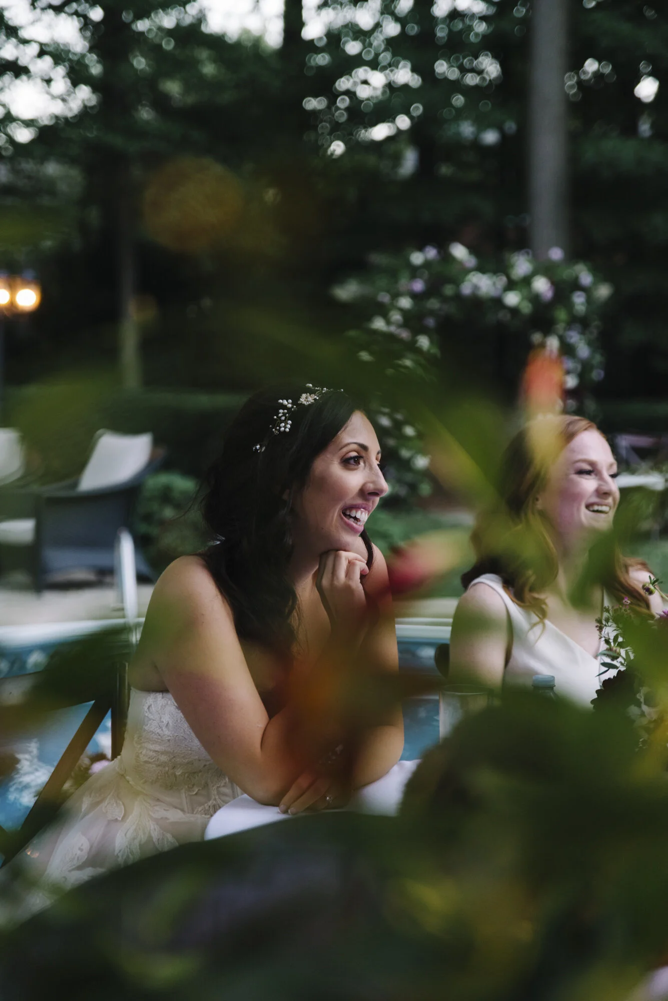 Candid photo of a bride smiling and emotional while listening to speeches at her intimate backyard wedding reception