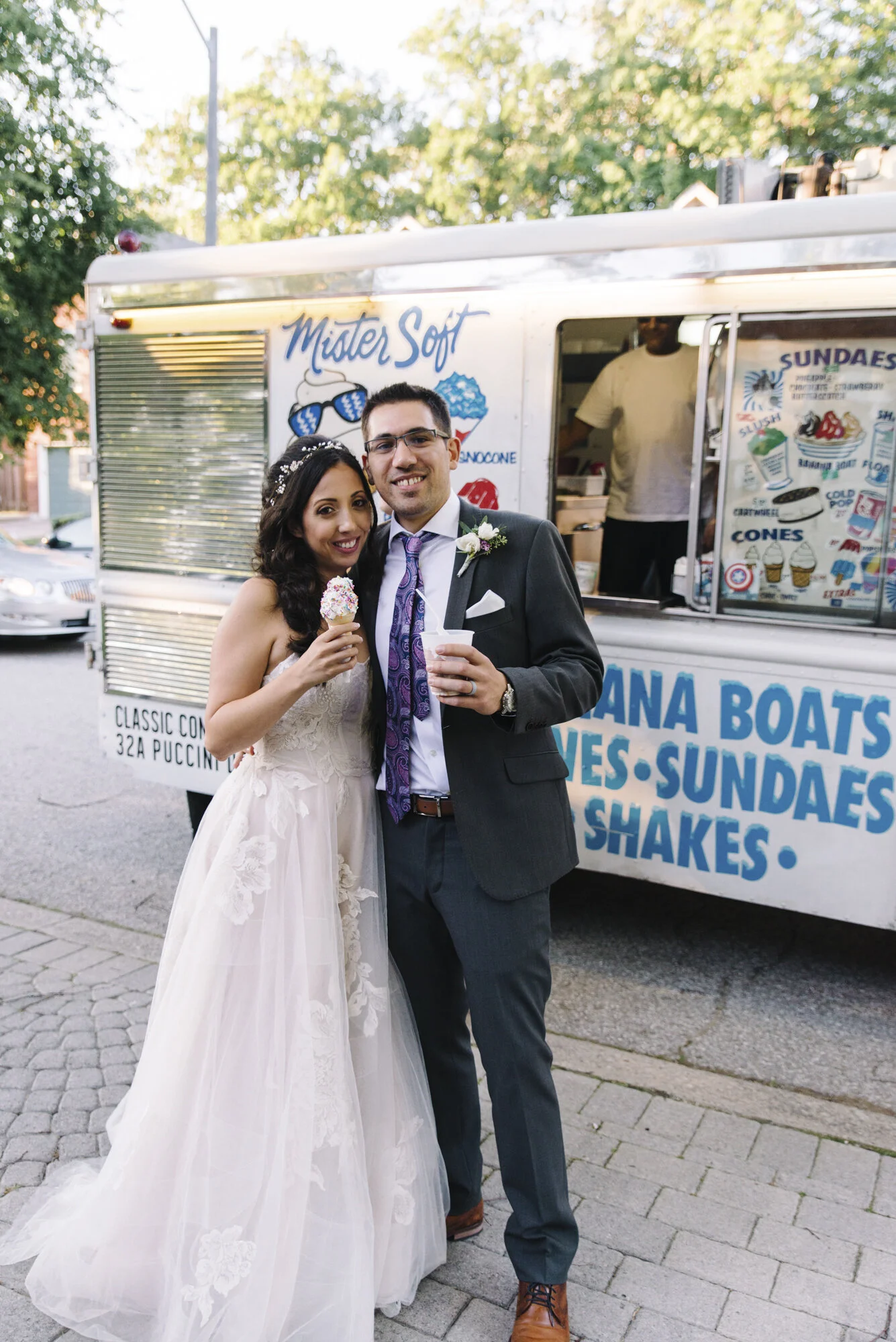 Candid photo of a bride and groom smiling at the camera with ice cream cones in front of their surprise ice cream truck at their backyard wedding in Mississauga