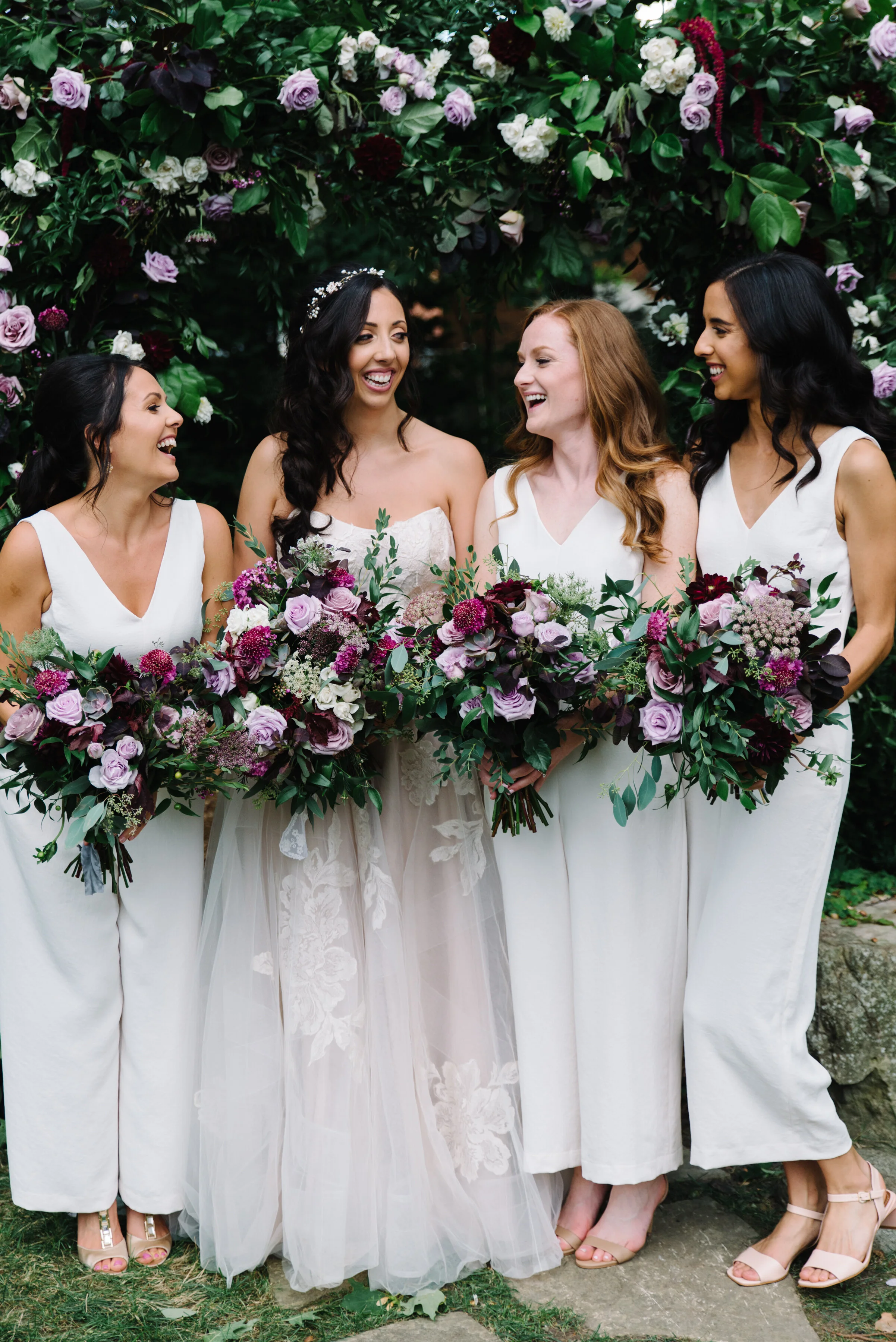 Bride and bridesmaids standing under a floral arch by The Paisley Rose at a backyard micro-wedding in Mississauga