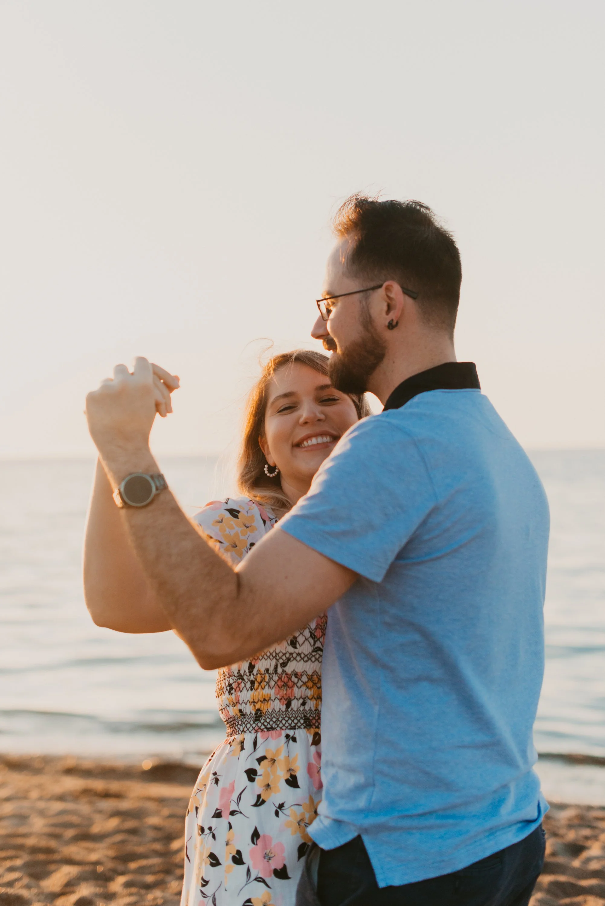 Candid photo of a couple dancing together on the beach during their sunrise engagement session at Woodbine Beach, Toronto