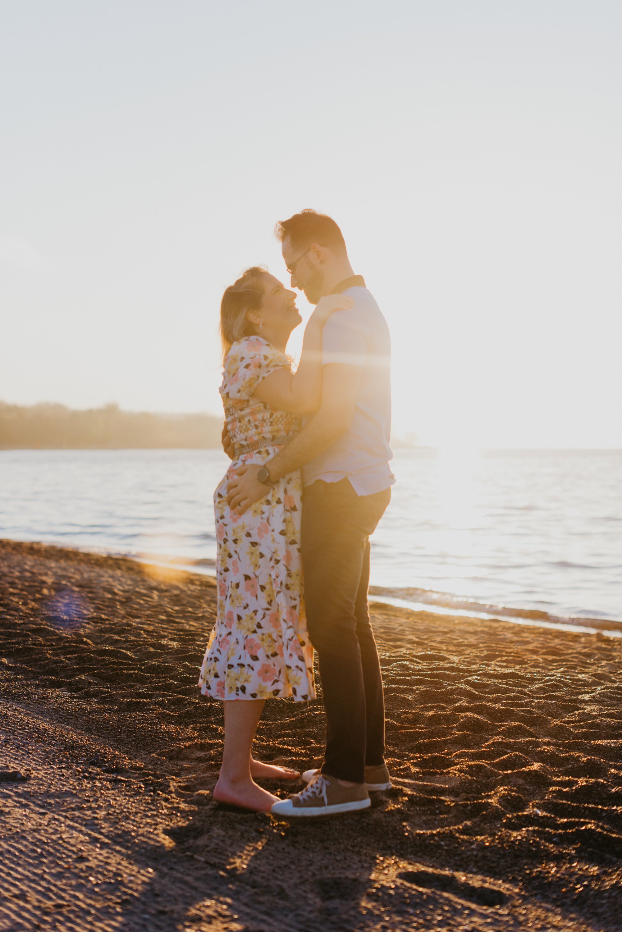 Couple holding each other on the beach as the sun rises behind them during their engagement session at Woodbine Beach, Toronto
