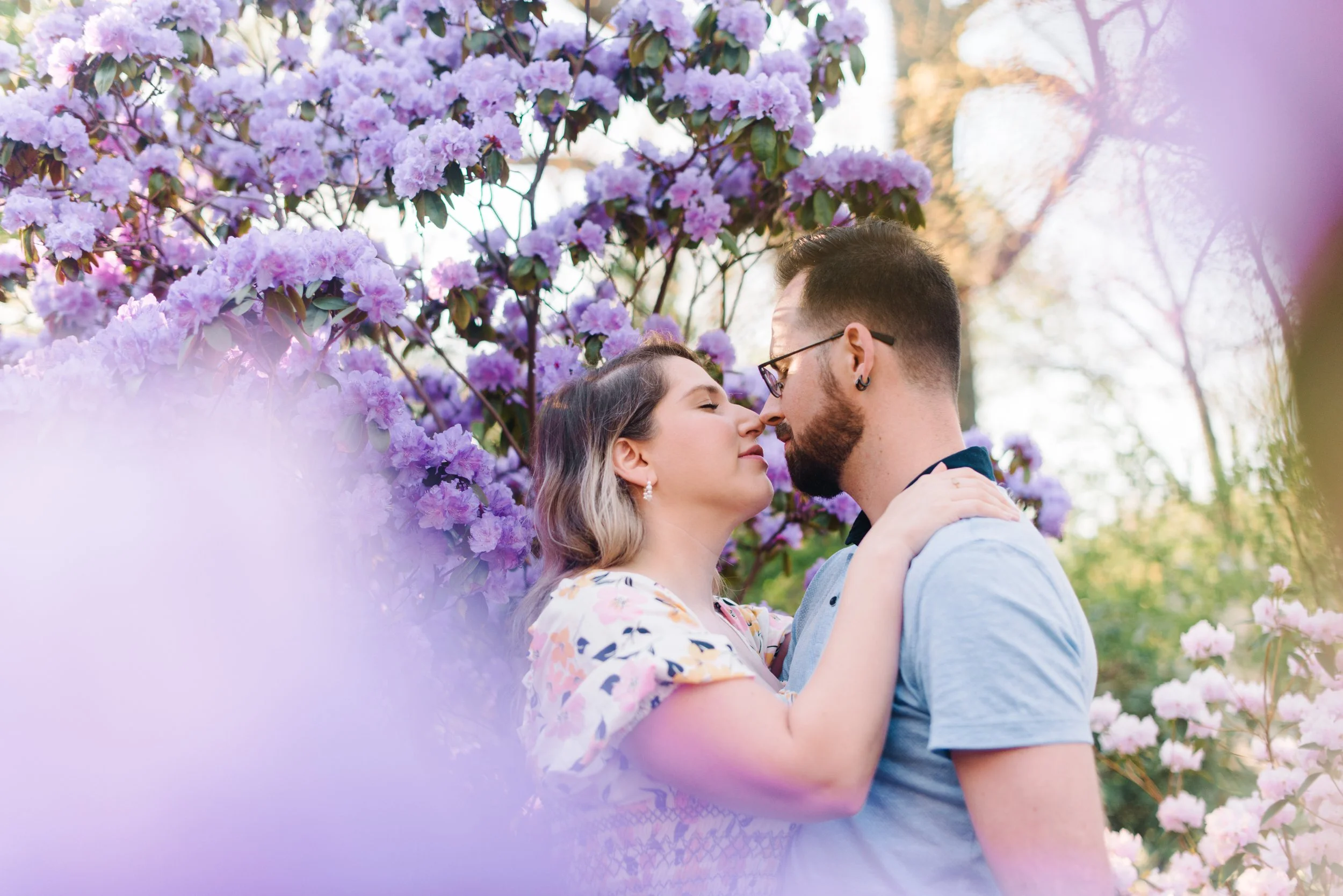Romantic photo of a couple in a lilac bush moments before kissing during their engagement session at Woodbine Beach, Toronto