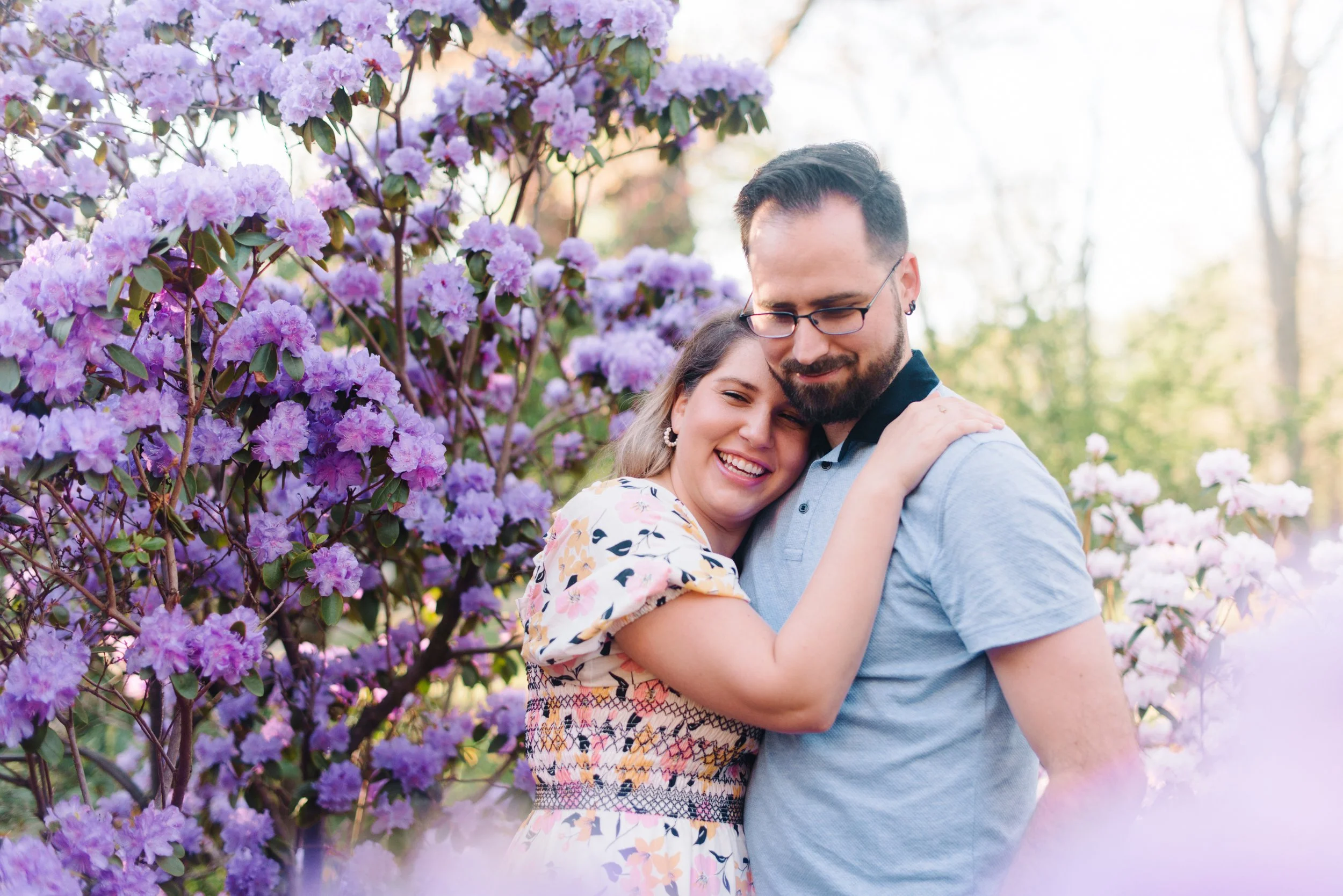 Candid photo of a couple laughing together in a lilac bush during their sunrise engagement session in Toronto