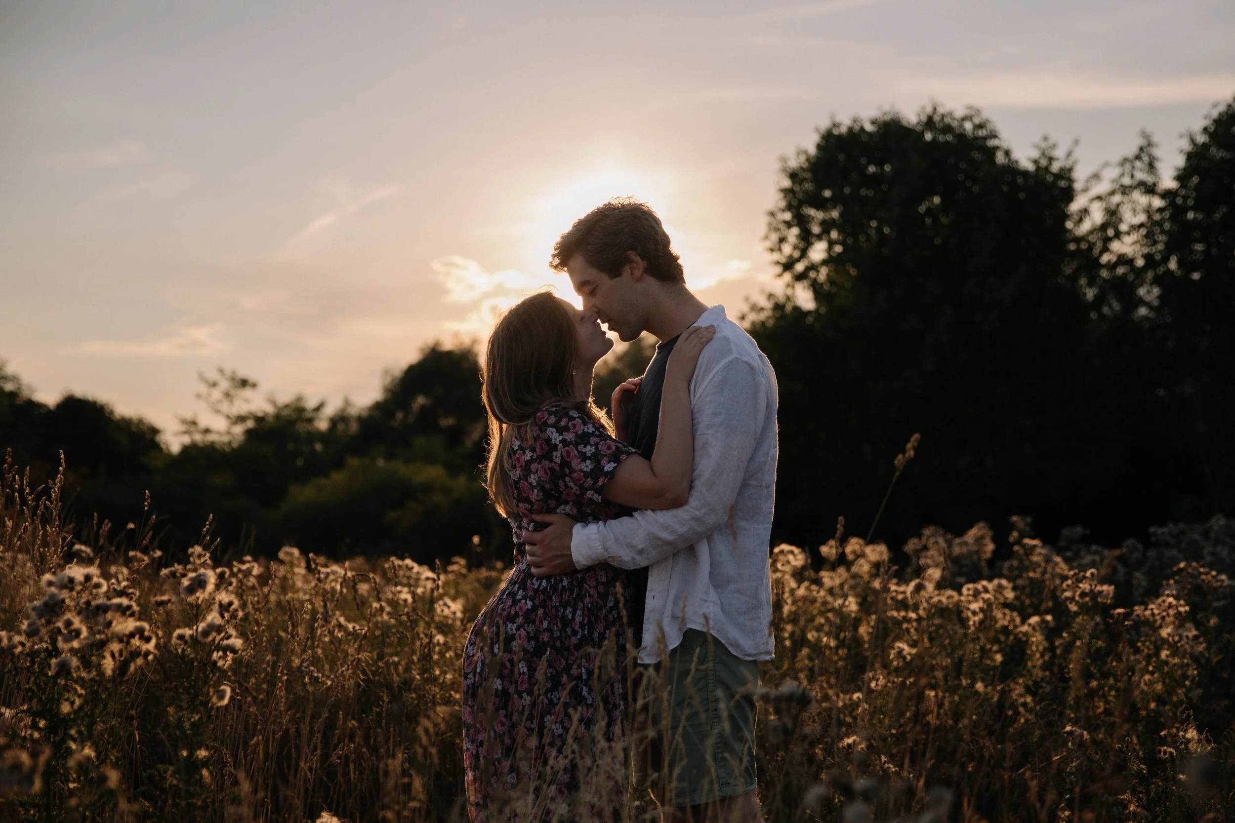 Editorial inspired engagement photo of a couple kissing in a field at sunset, beautifully backlit with dreamy golden light in Toronto