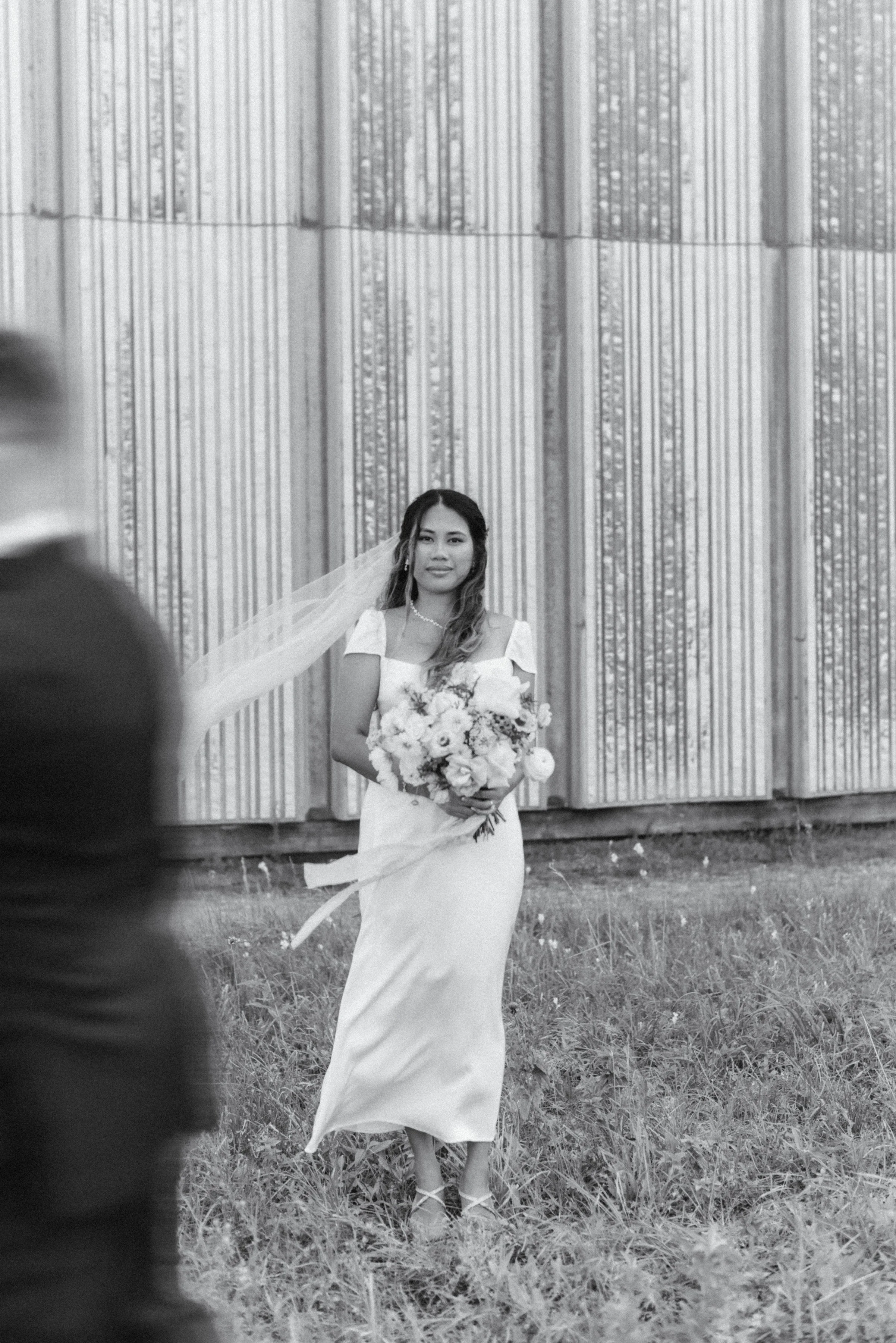 Black and white editorial portrait of a bride with the groom walking out of frame with motion blur at Toronto City Hall