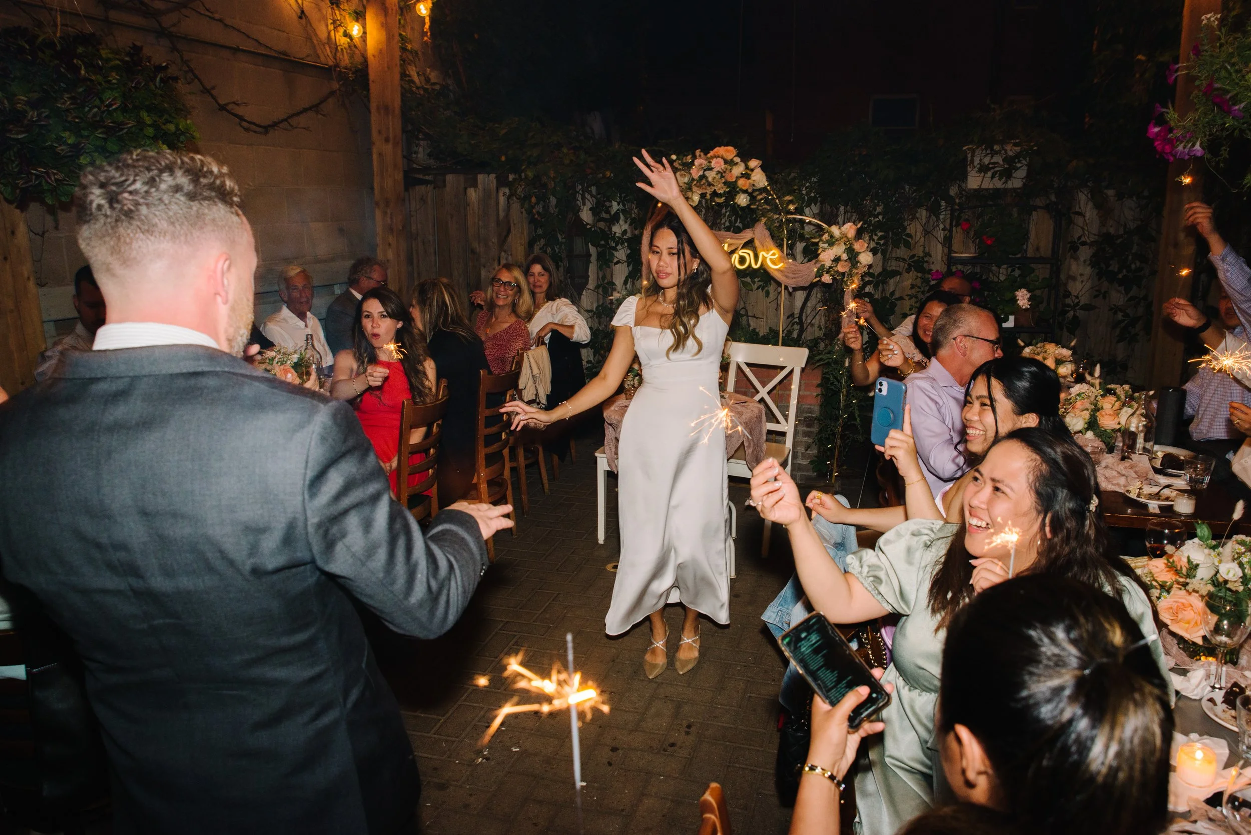 Candid photo of a bride and groom dancing at their reception as guests hold sparklers and cheer around them in Toronto