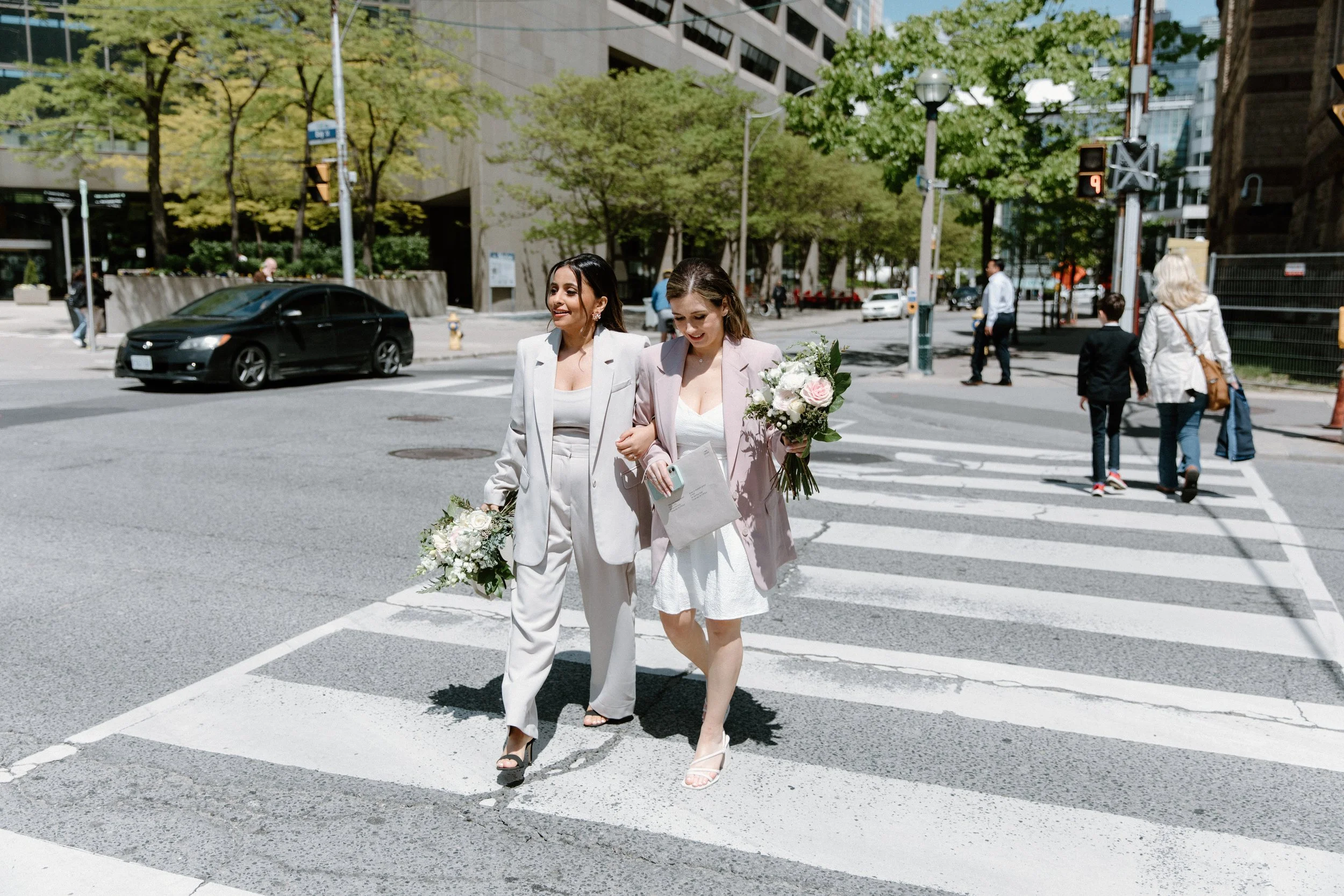 Documentary photo of two brides walking through downtown Toronto on their way to their City Hall elopement