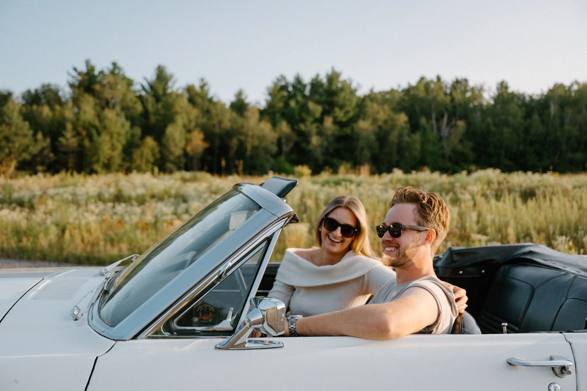 Candid moment of an engaged couple laughing together in the front seats of a vintage Mustang in Pontypool, Ontario
