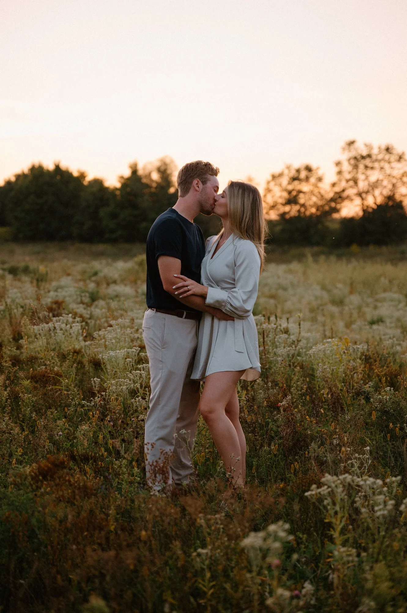 Engaged couple kissing in an open field at sunset during their engagement session near Peterborough, Ontario