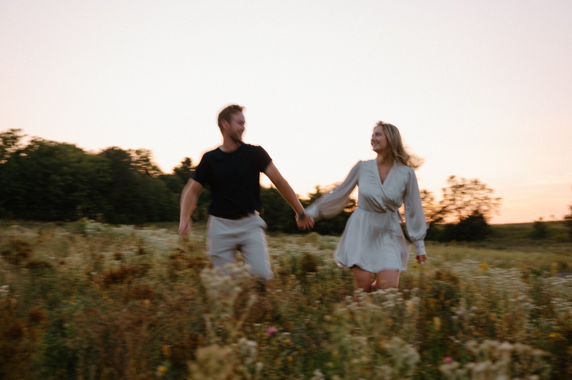 Engaged couple running and laughing together in a field at golden hour during their Kawartha engagement session