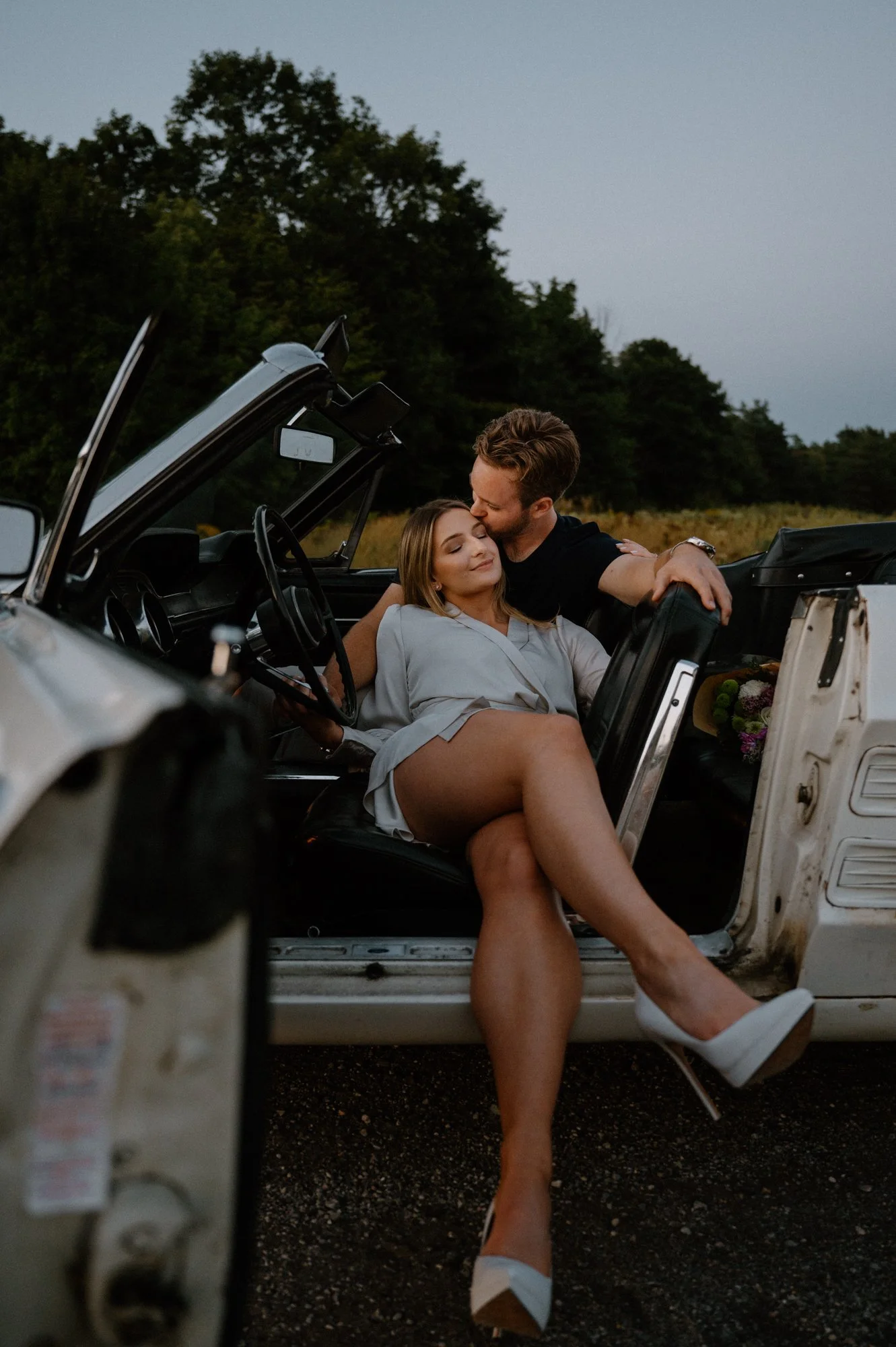 A couple romantically lay in their vintage Mustang, kissing, for an editorial engagement session