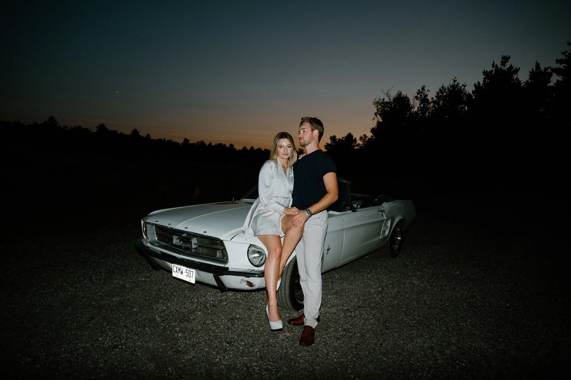 Modern flash photography engagement portrait of a couple on the hood of a vintage Mustang in the Kawarthas