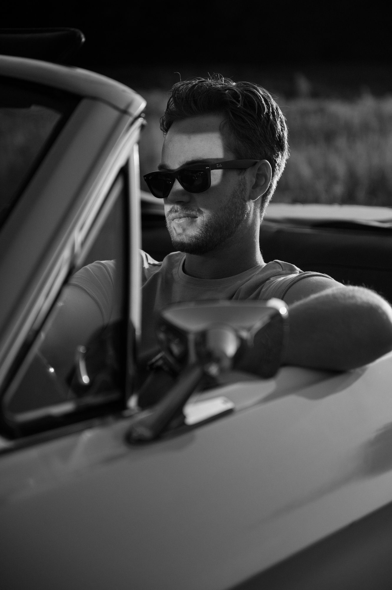Cinematic black and white portrait of a groom to be sitting in the driver's seat of a vintage Mustang