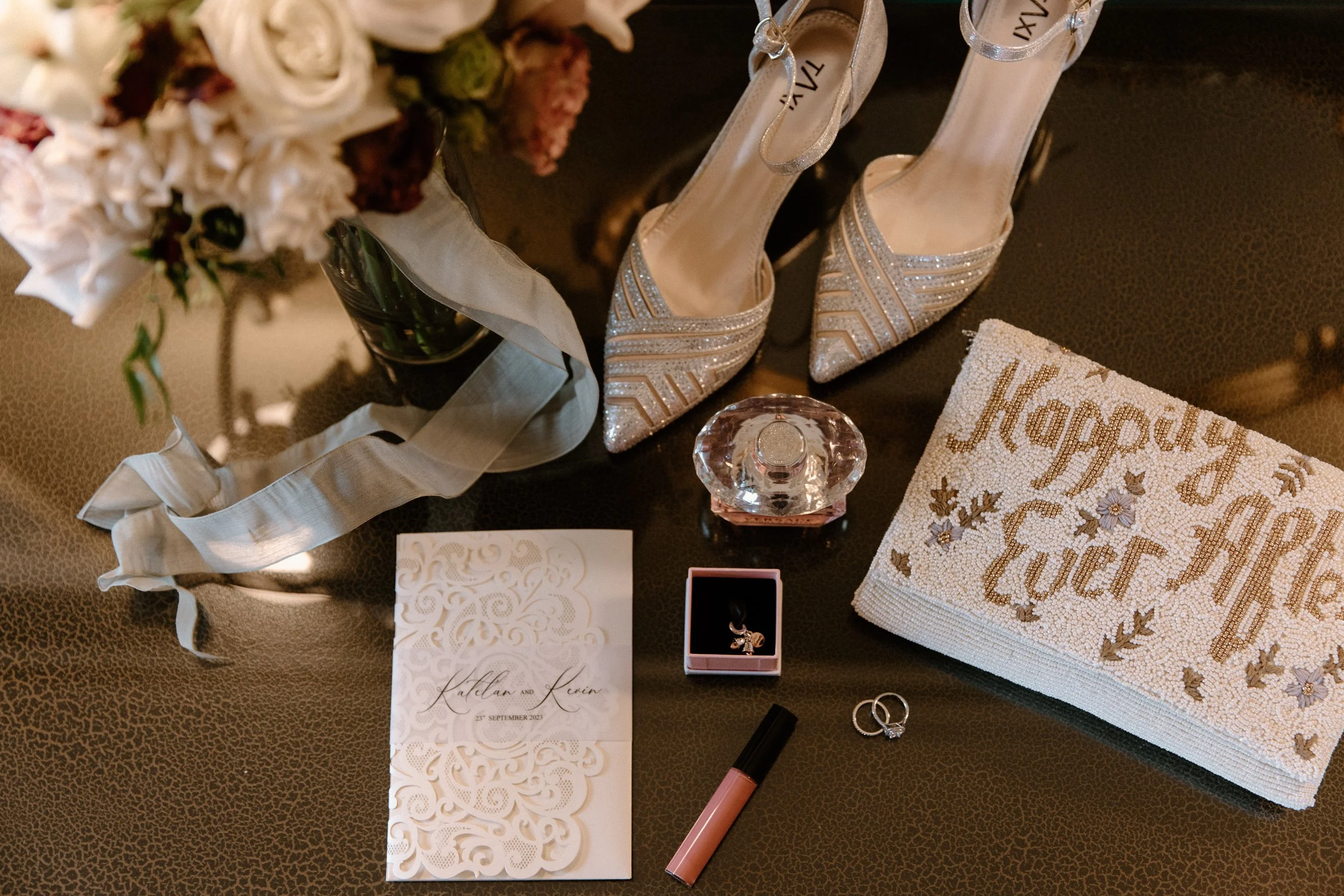 Trendy editorial flat lay of bridal details including vows, shoes, purse, lipstick, and rings on a Toronto wedding day