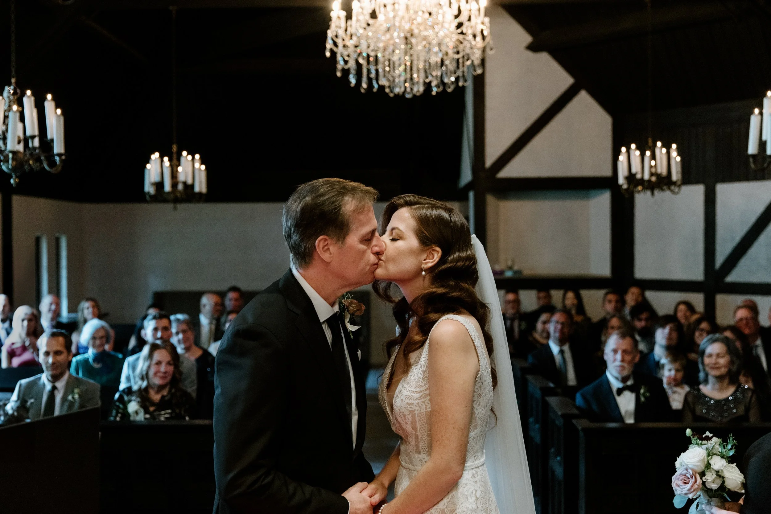 Candid photo of a bride and groom sharing their first kiss during their Toronto wedding ceremony with joyful guests in the background