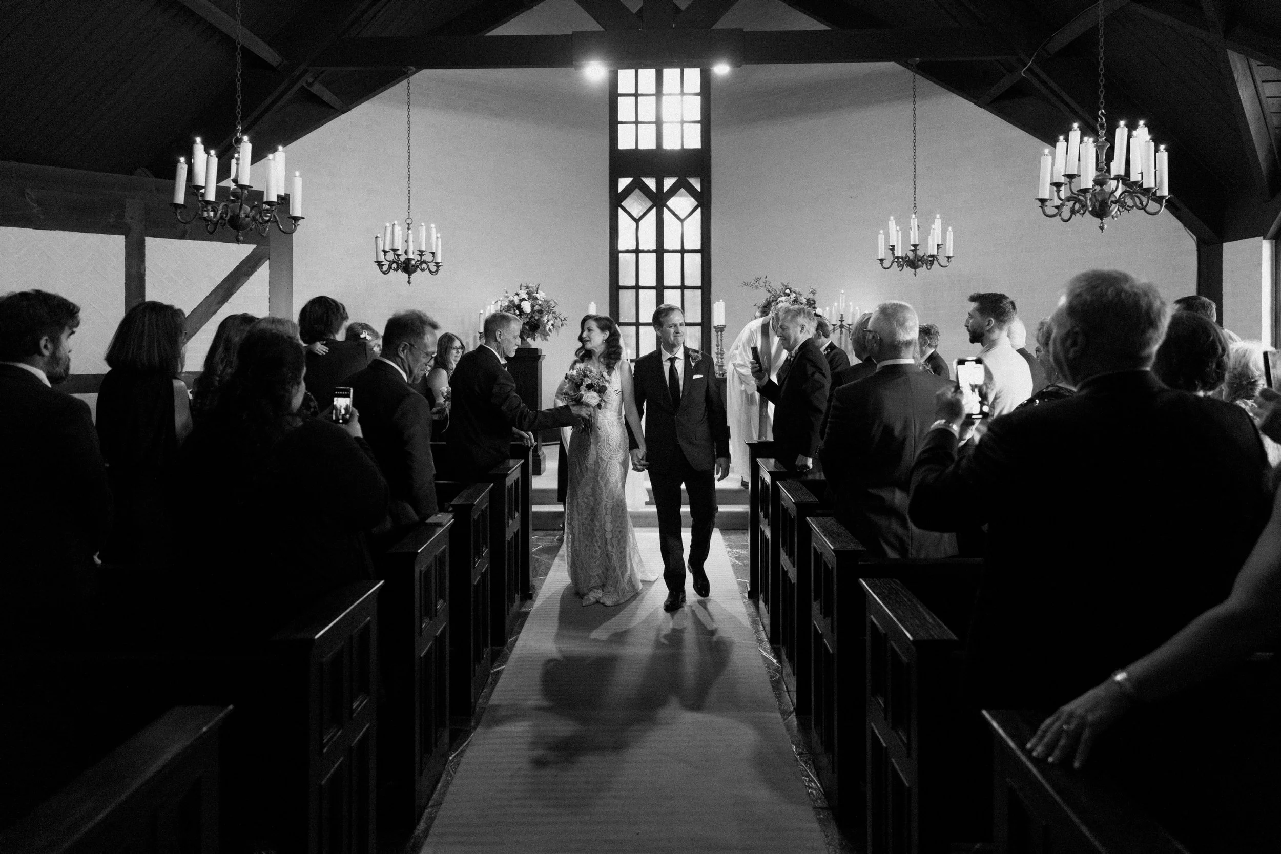 Black and white photo of a bride and groom walking down the aisle during their recessional with guests cheering around them at their Toronto wedding
