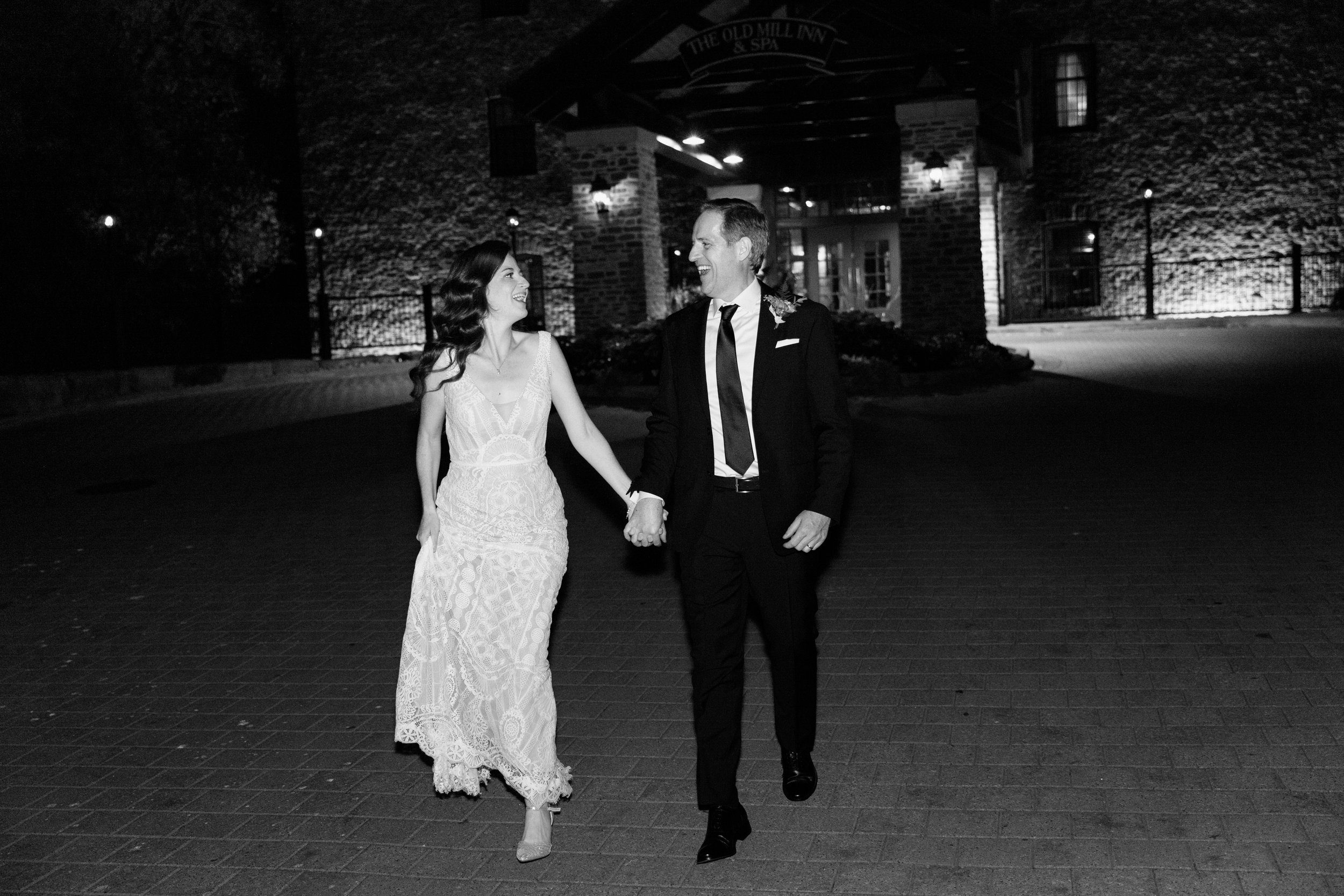 Black and white editorial flash photo of a bride and groom walking outside their Toronto wedding venue at night