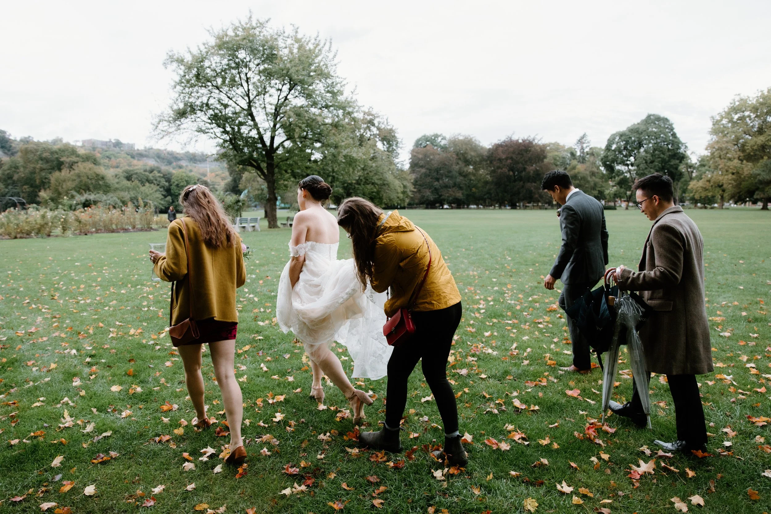 Candid photo of bride, groom, and friends walking through Gage Park in the rain on their Hamilton wedding day