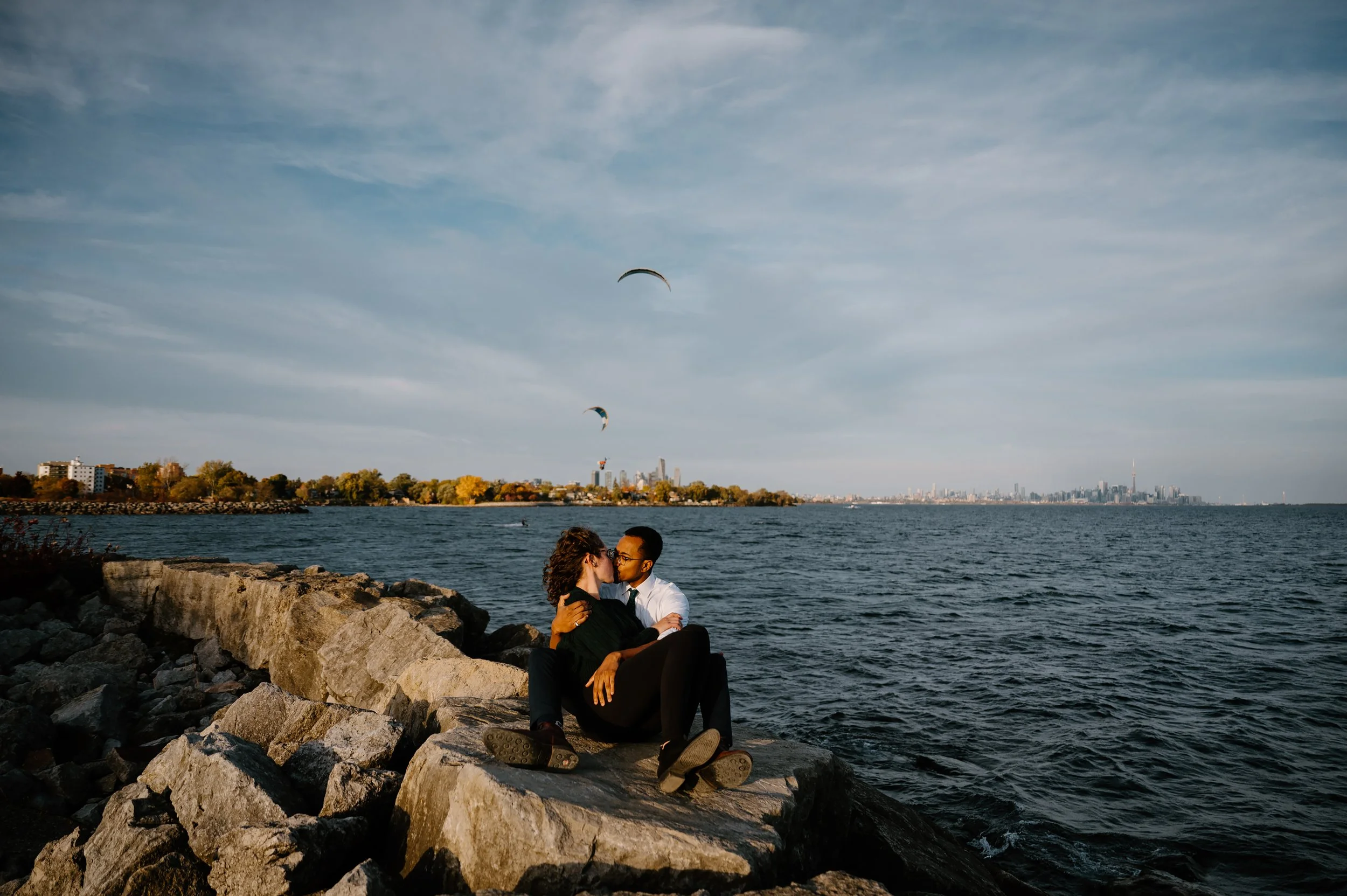Engaged couple sitting together at the waterfront with the Toronto skyline visible in the background