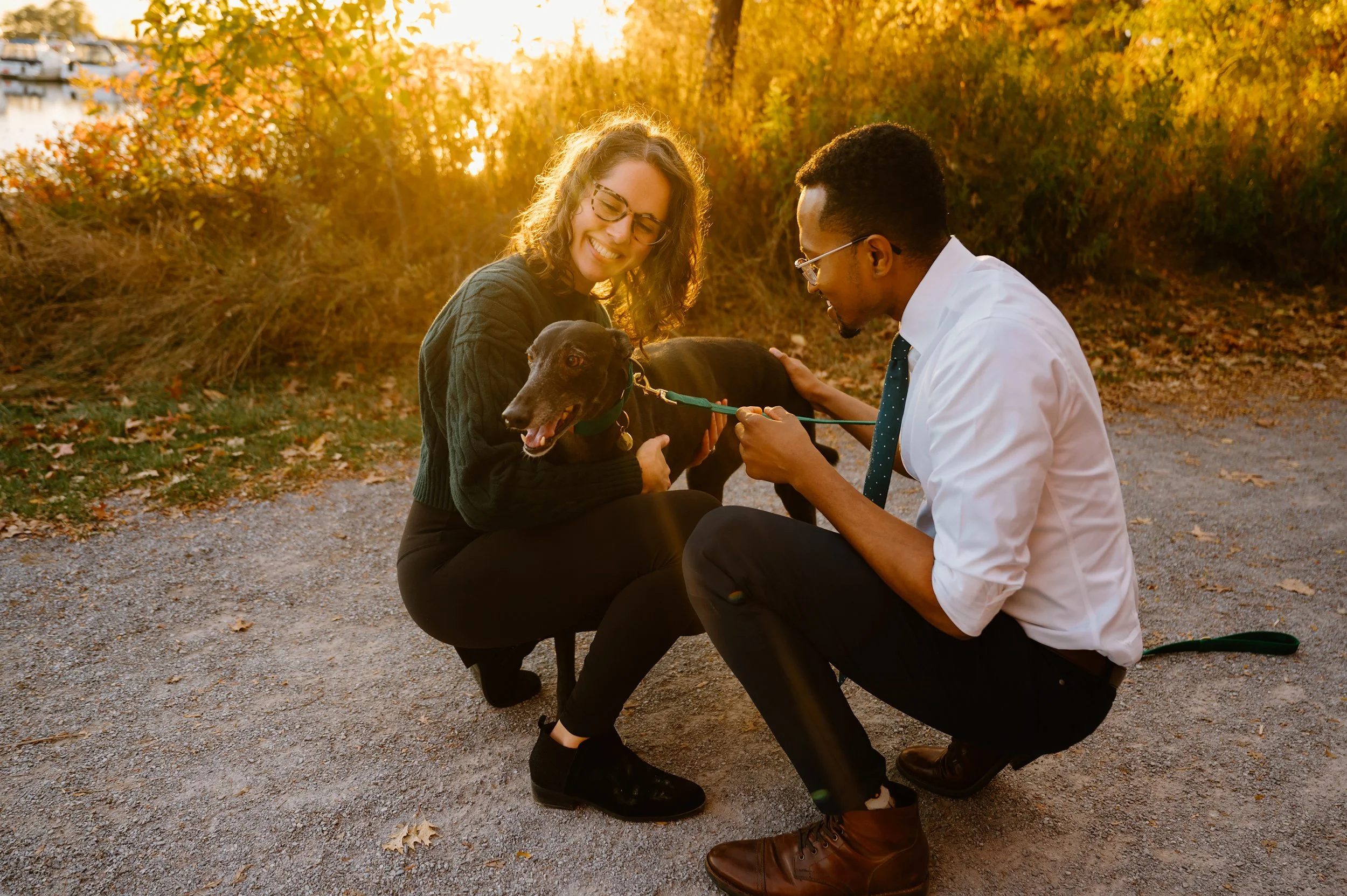 Romantic engagement photo of a couple smiling with their dog, warm golden light glowing behind them