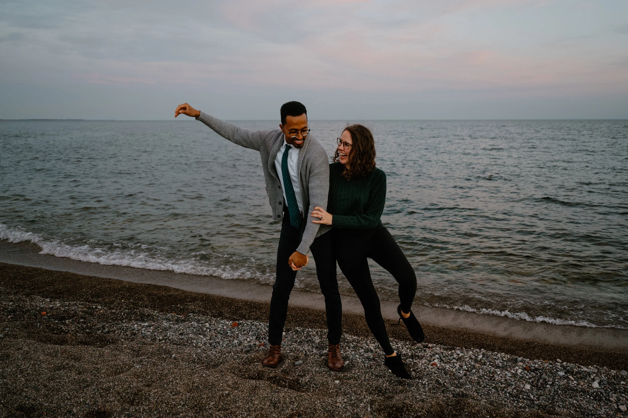 Playful and candid photo of an engaged couple on the beach during a sunset engagement session in a Vancouver-like coastal setting