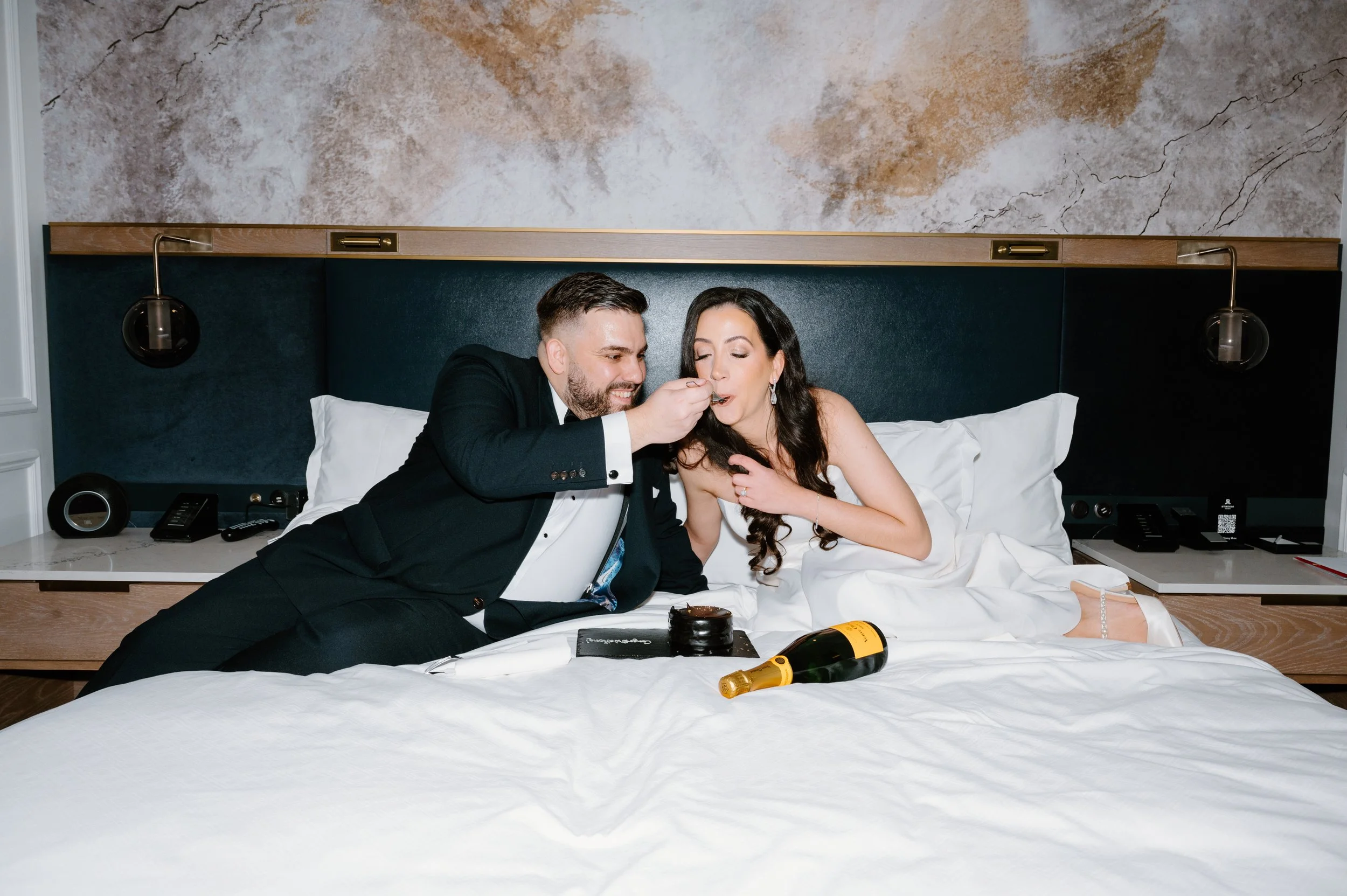 Couple eating cake on a hotel bed at the St. Regis Toronto, photographed with editorial flash