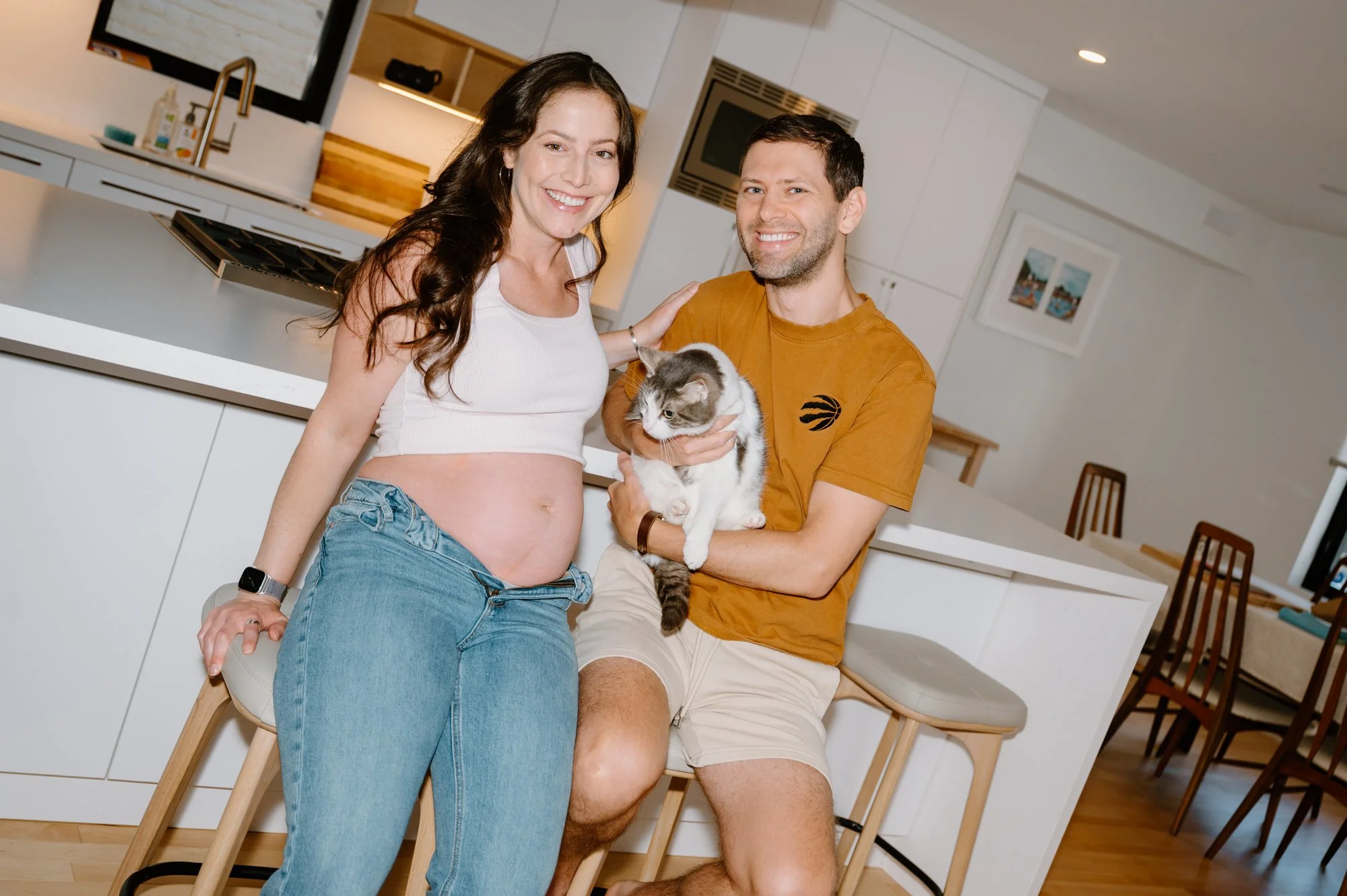 Modern at-home maternity photo of a couple sitting in the kitchen with their cat in Toronto