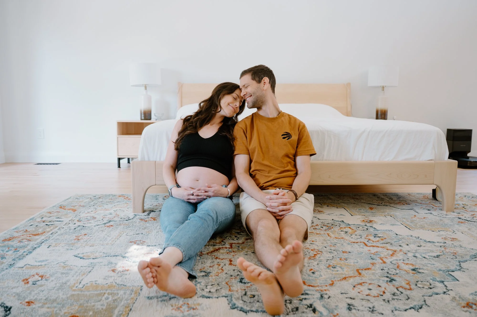 Modern at-home maternity portrait of a couple sitting together in their bedroom in Toronto