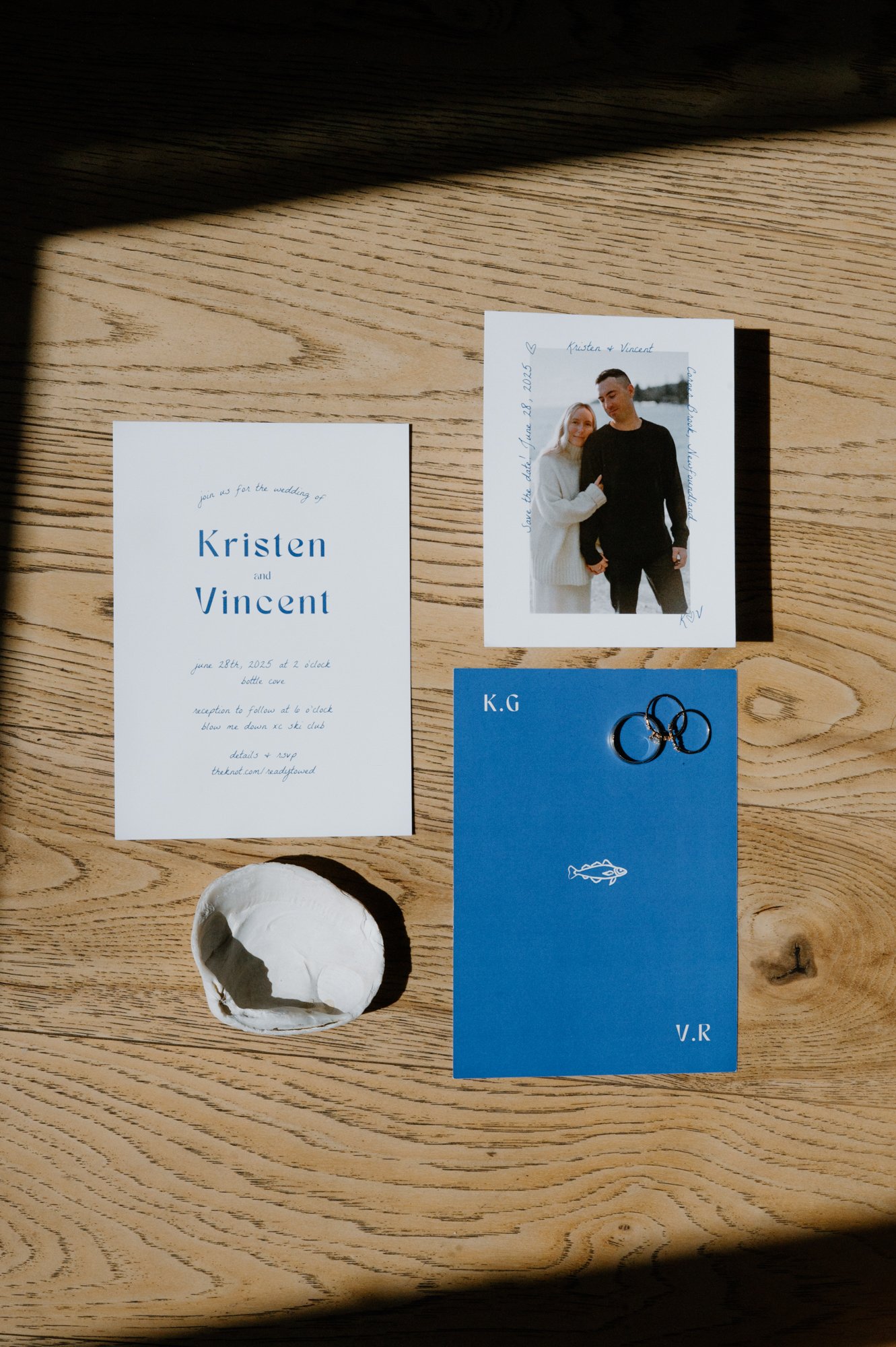 Flat lay of a custom designed wedding invitation suite alongside Bluboho rings at a destination wedding in Corner Brook, Newfoundland