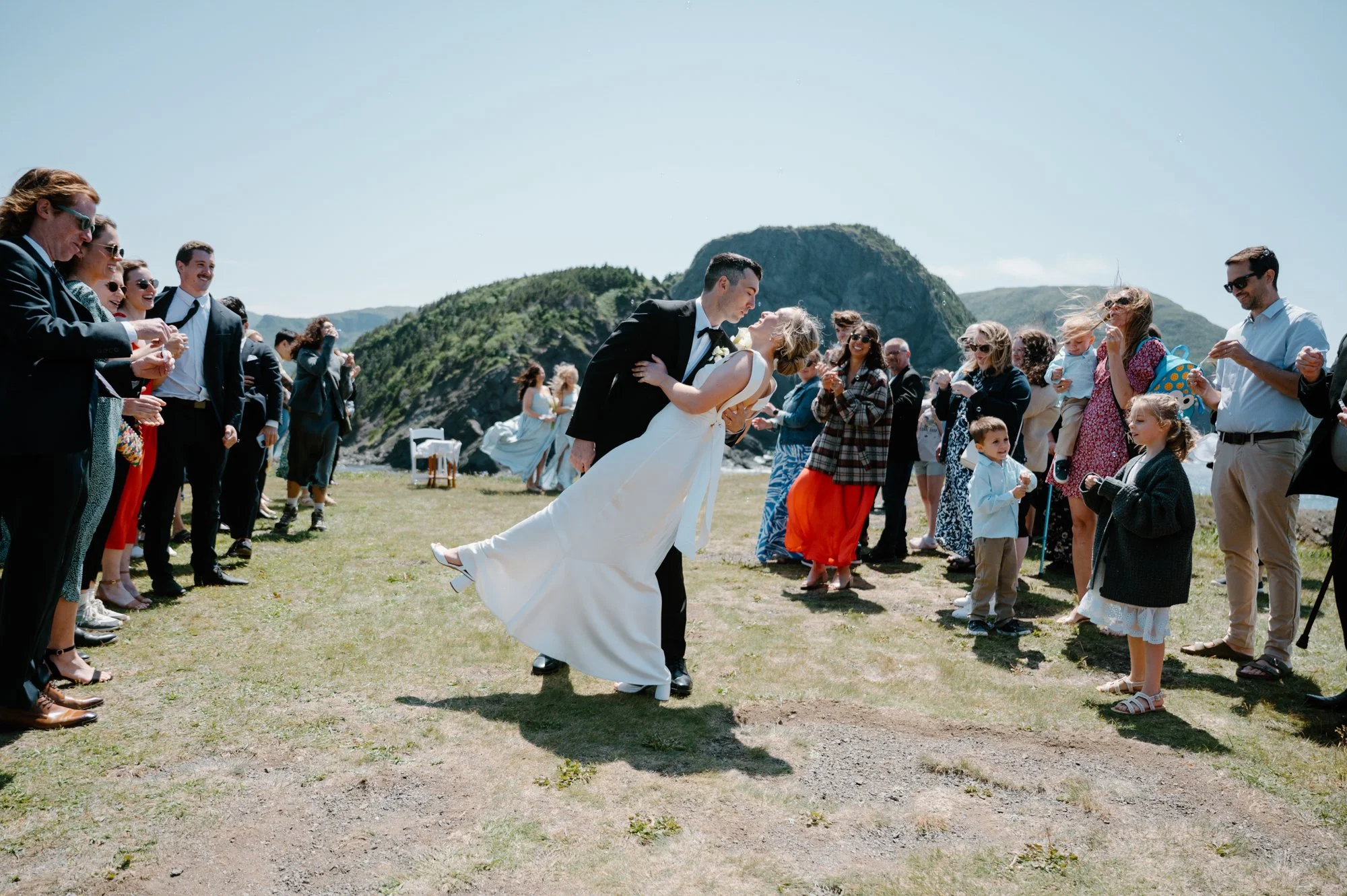 Joyful candid of a bride and groom stopping for a dip and kiss during their recessional as guests cheer around them