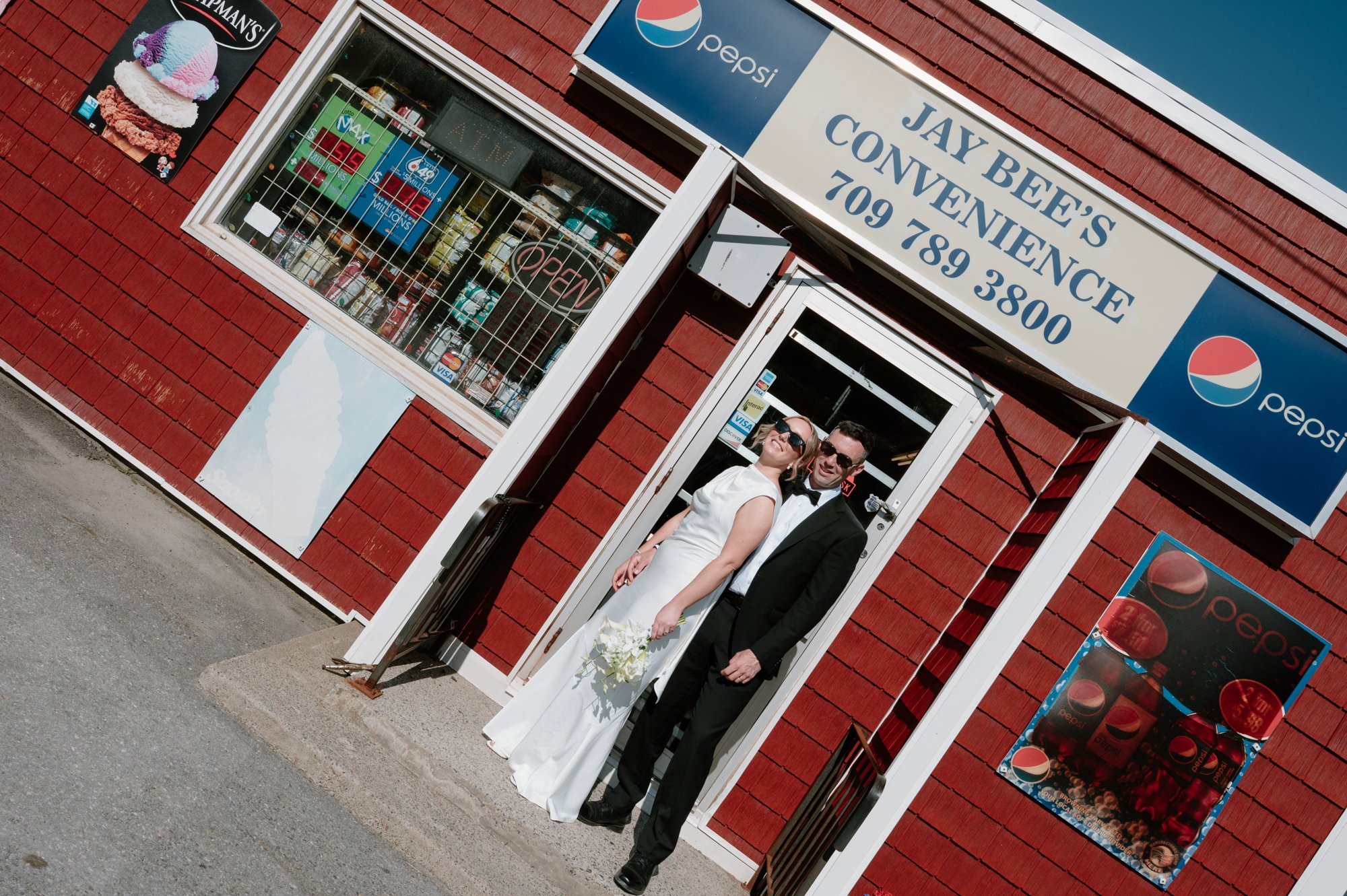 Chic editorial inspired portrait of a bride and groom in front of a local corner store during their destination wedding in Corner Brook, Newfoundland