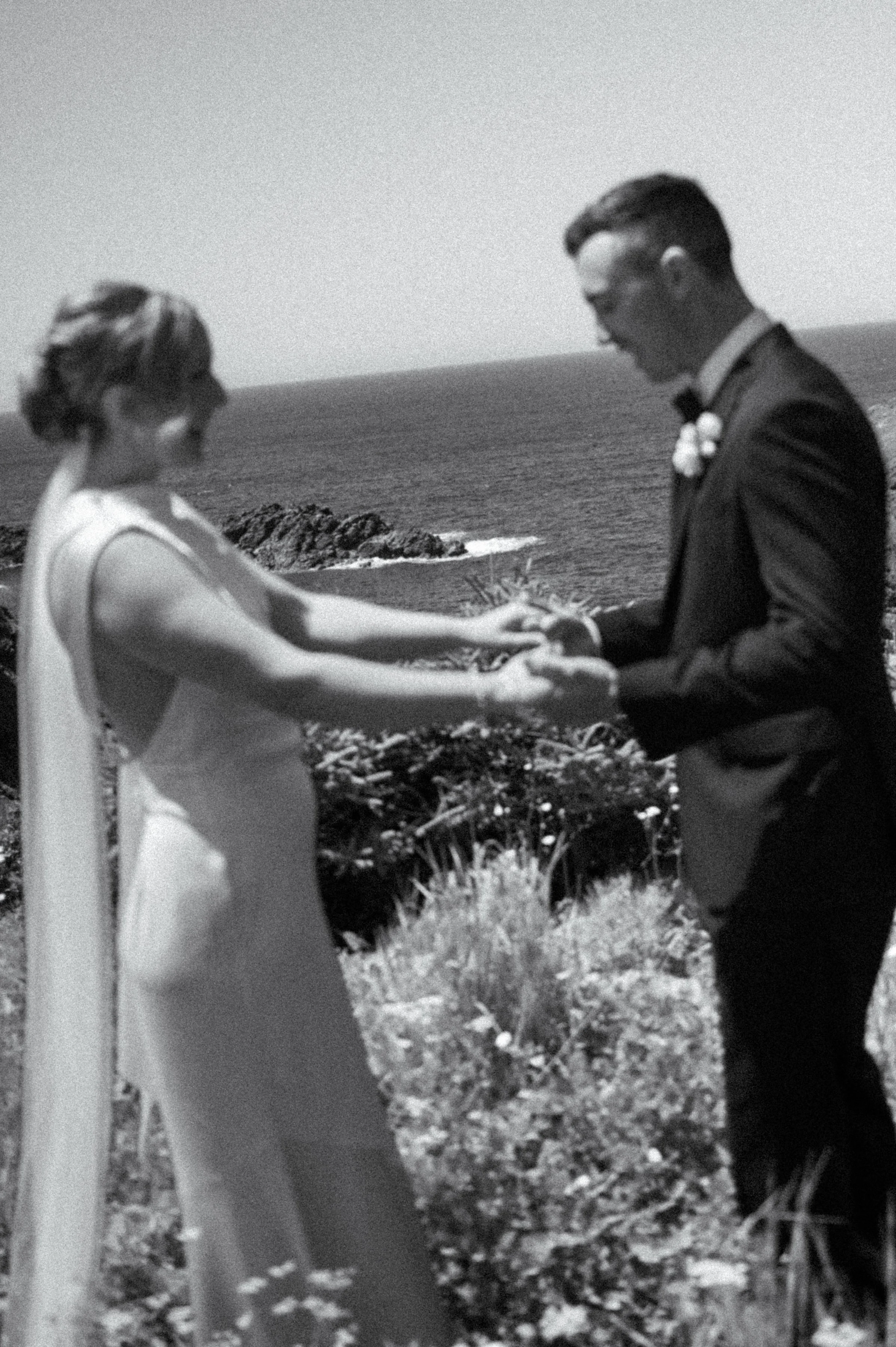 Black and white film inspired editorial portrait with bride and groom softly out of focus and Bottle Cove dramatically in the background
