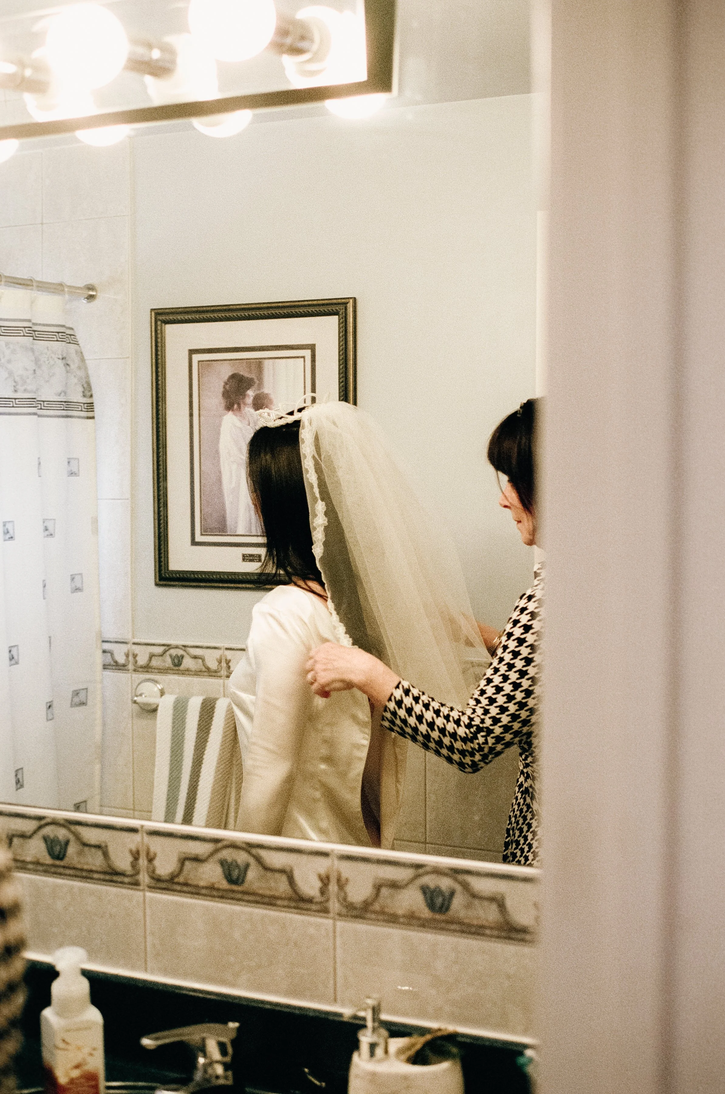 Candid film photograph captured as a mirror reflection of a mother helping her daughter with her veil before an at-home civil ceremony in Vancouver