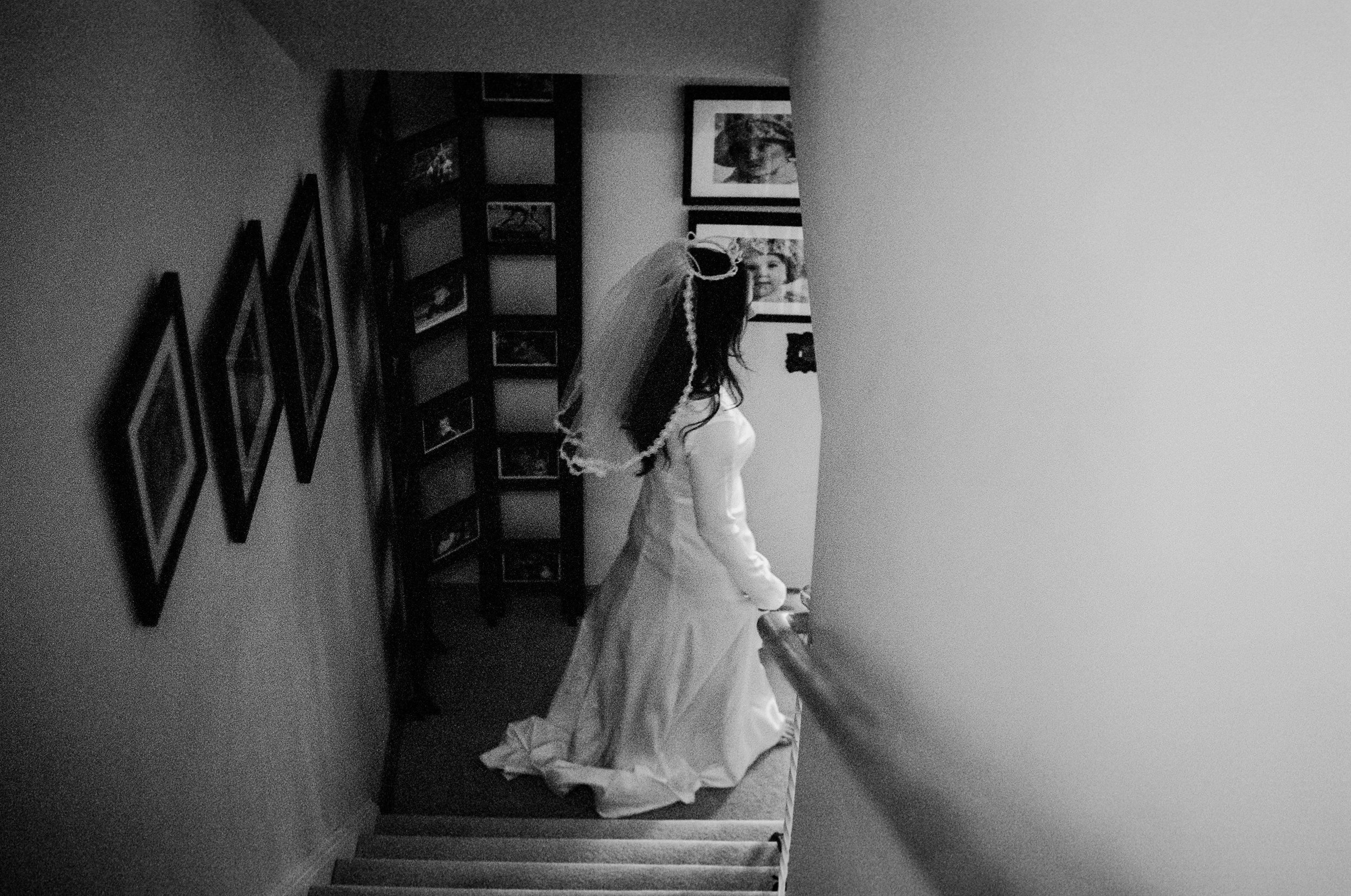 Black and white film photograph of a bride in her wedding dress walking downstairs before her at-home civil ceremony in Vancouver