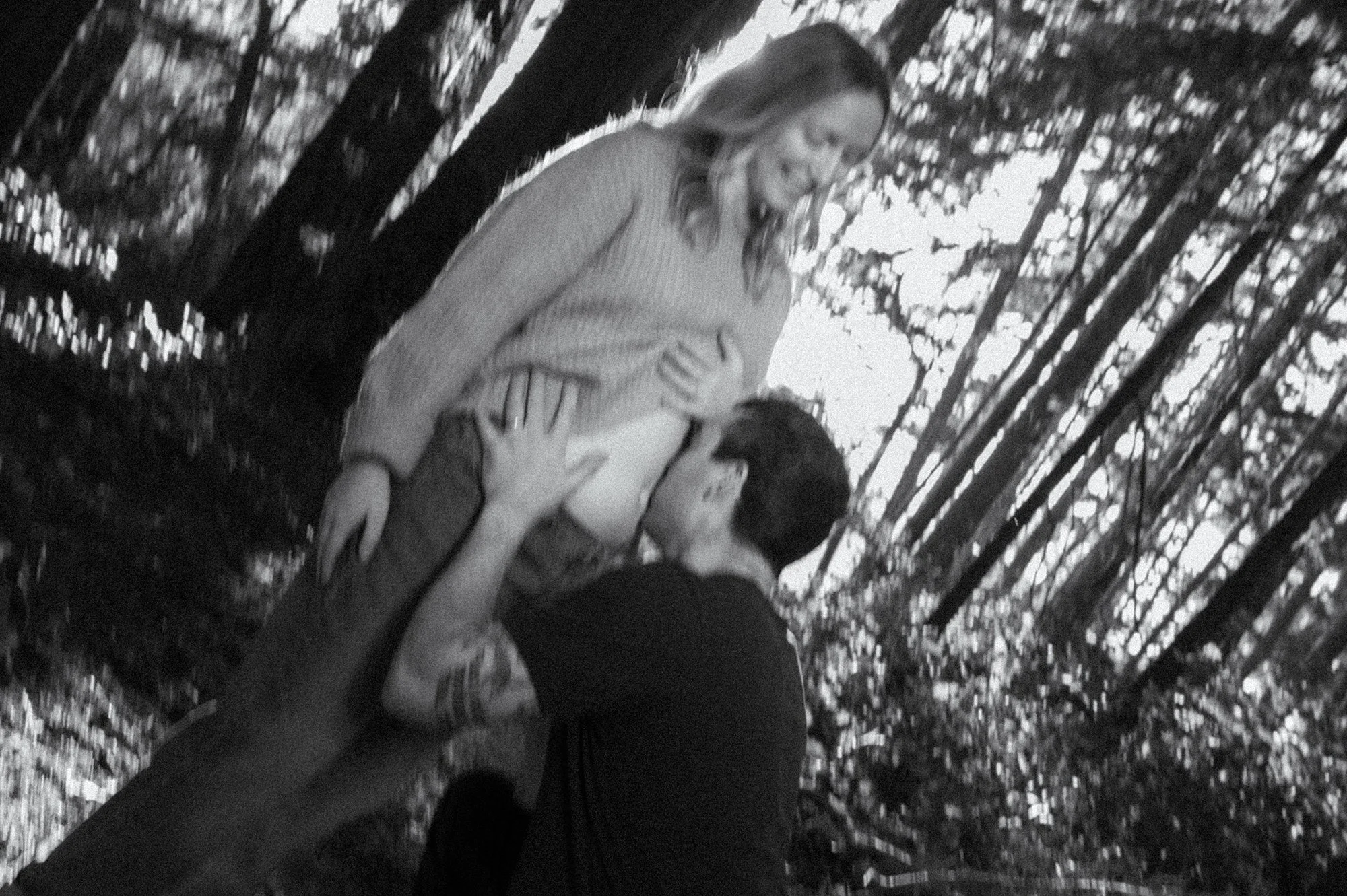 Black and white film photograph with motion blur of a partner kissing a pregnancy bump during a maternity session near Tofino, BC