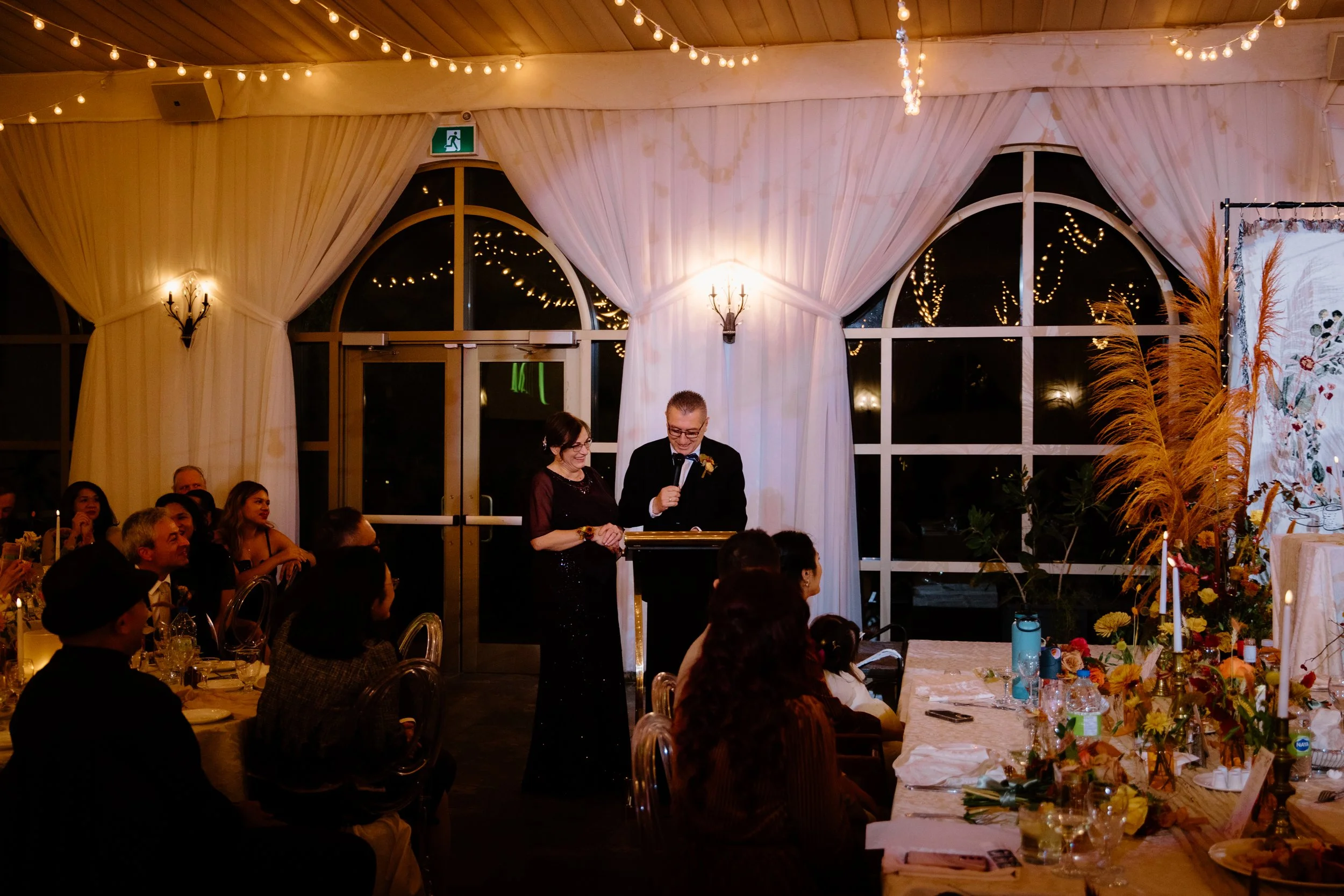 Candid photo of the groom's parents making a speech during dinner at their Caledon wedding reception
